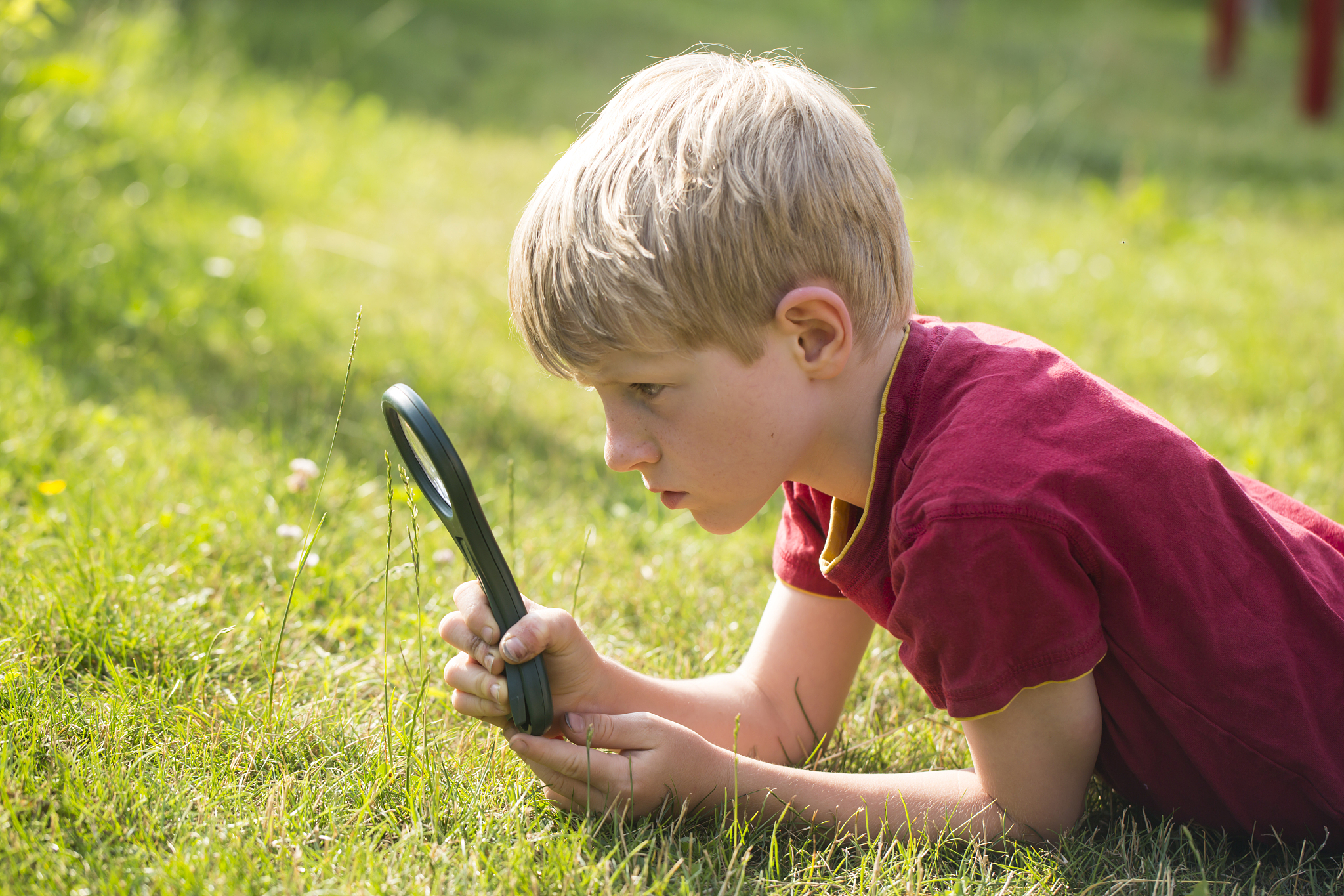 germany, bavaria, boy looking through magnifying glass in garden