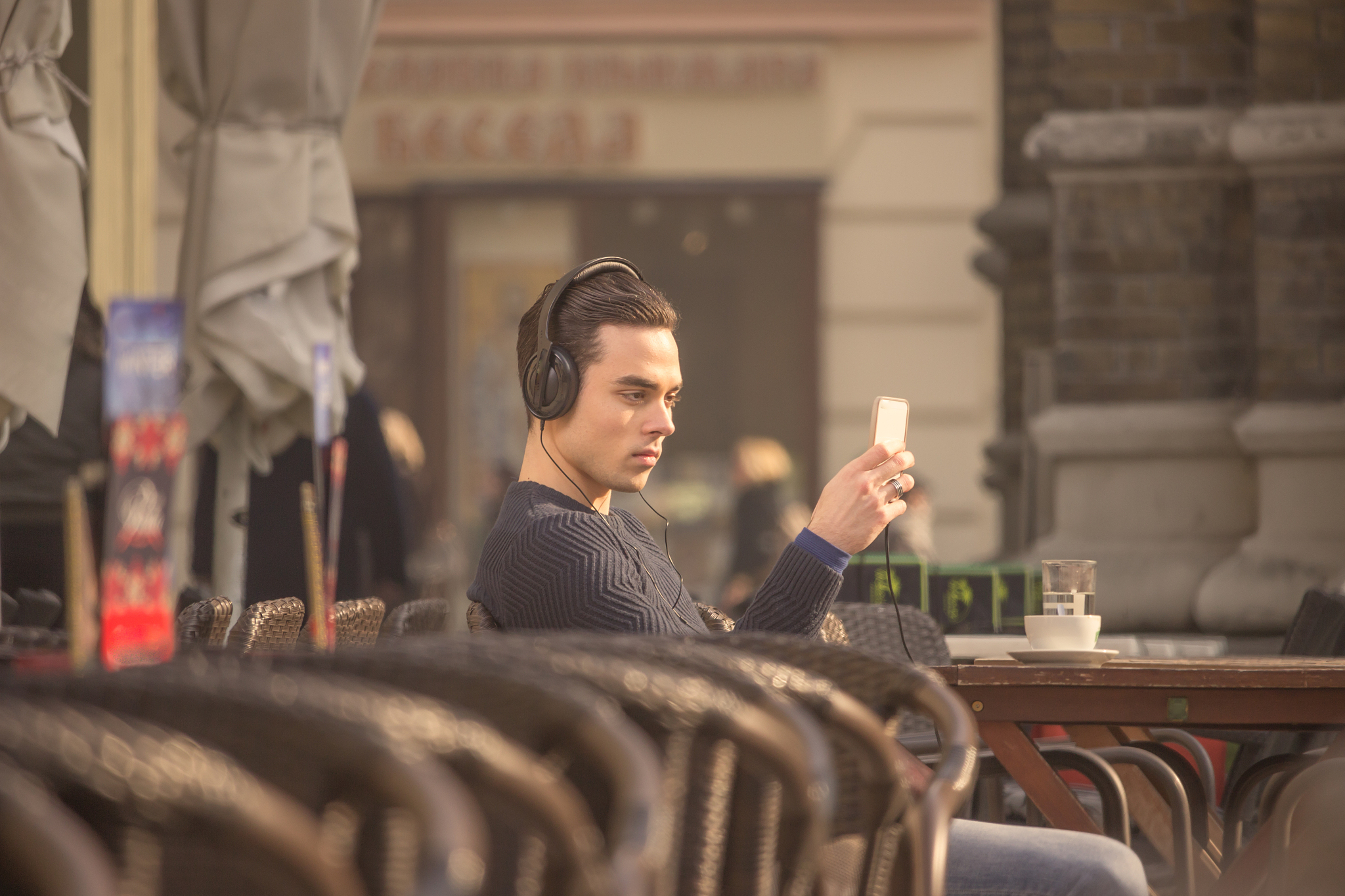 young man using smartphone headphones outdoors coffee table chai