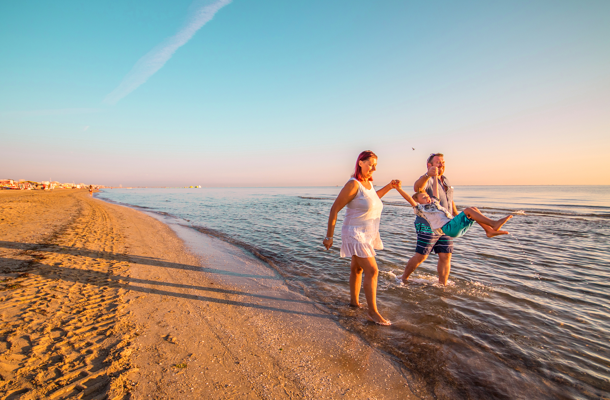 family at beach against sky during sunset
