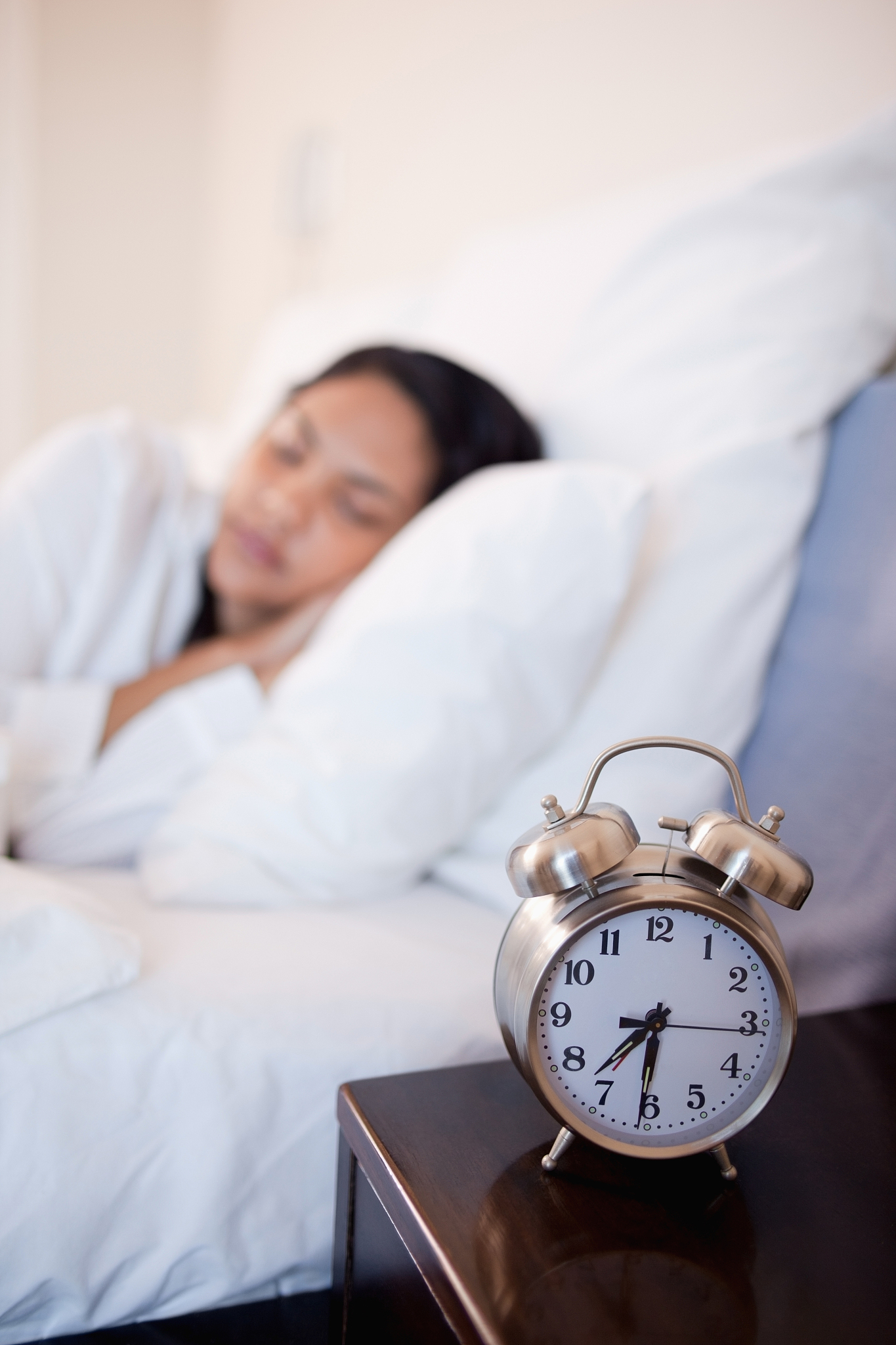 alarm clock next to bed in which woman is sleeping