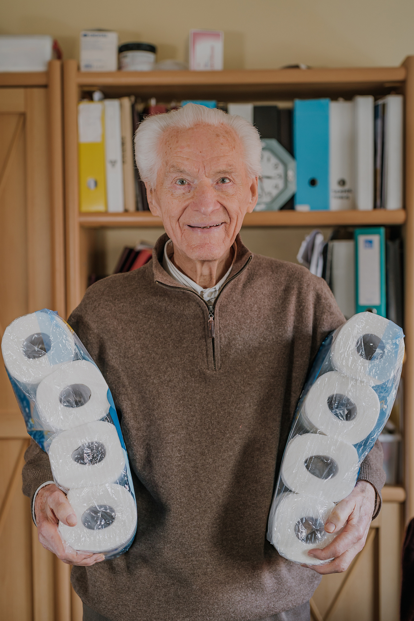 old man holding two packs of toilet paper