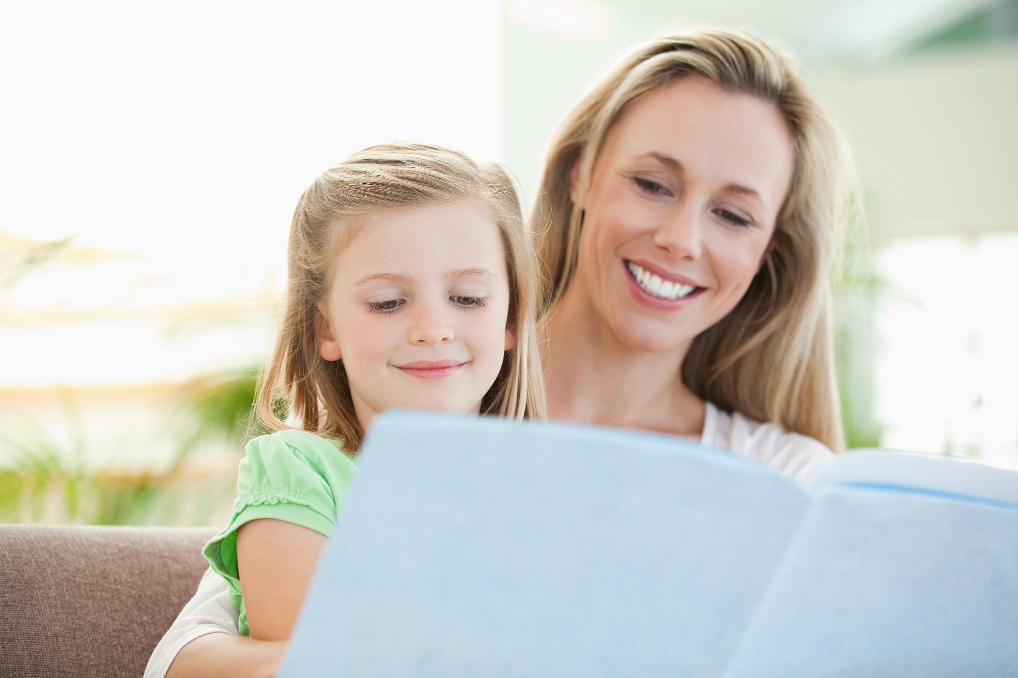 mother and daughter reading a magazine together on the couch
