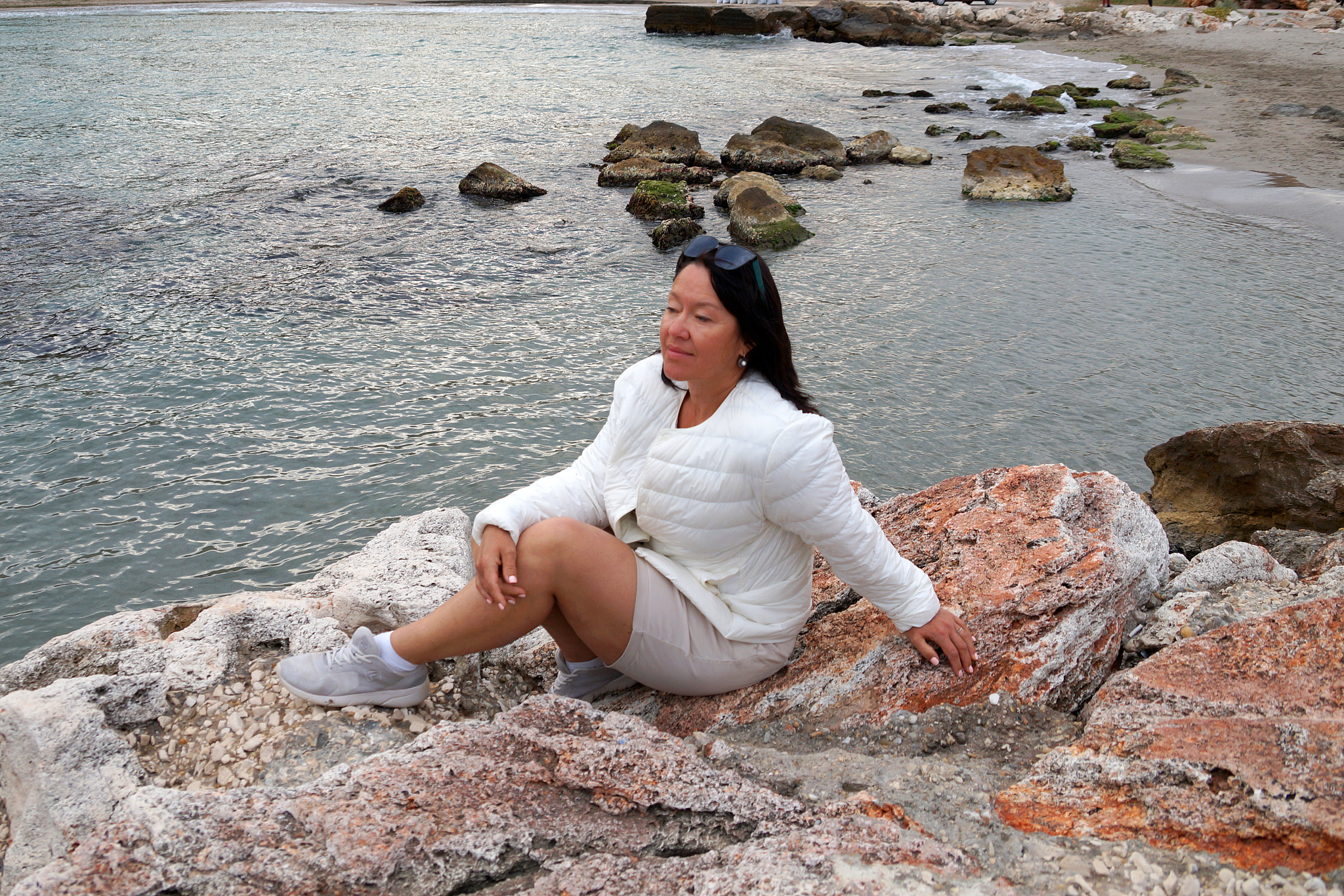asian woman sits on the wild seashore and looks into the distanc