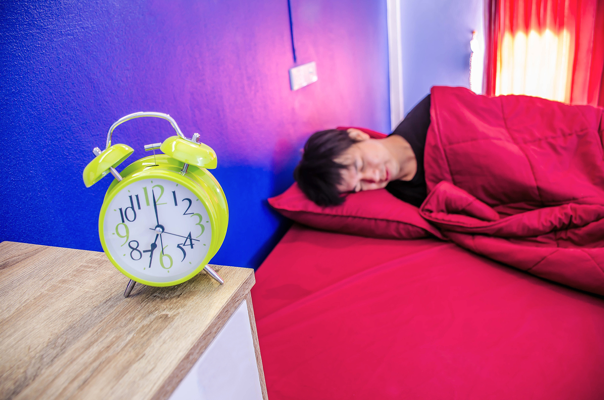young man sleeping on a comfortable bed covered with a red blank
