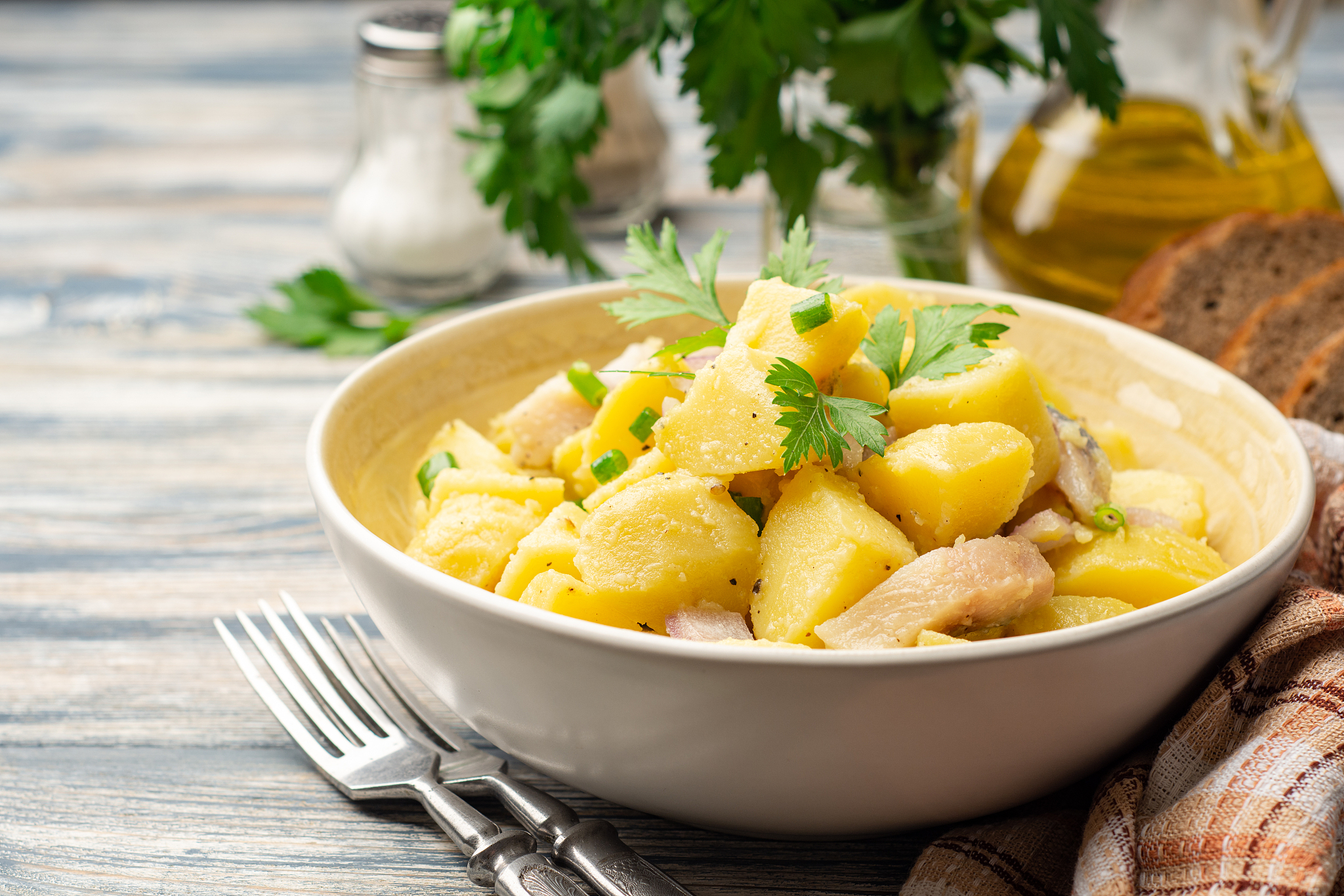 potato salad with salted herring, onion and parsley in bowl on r
