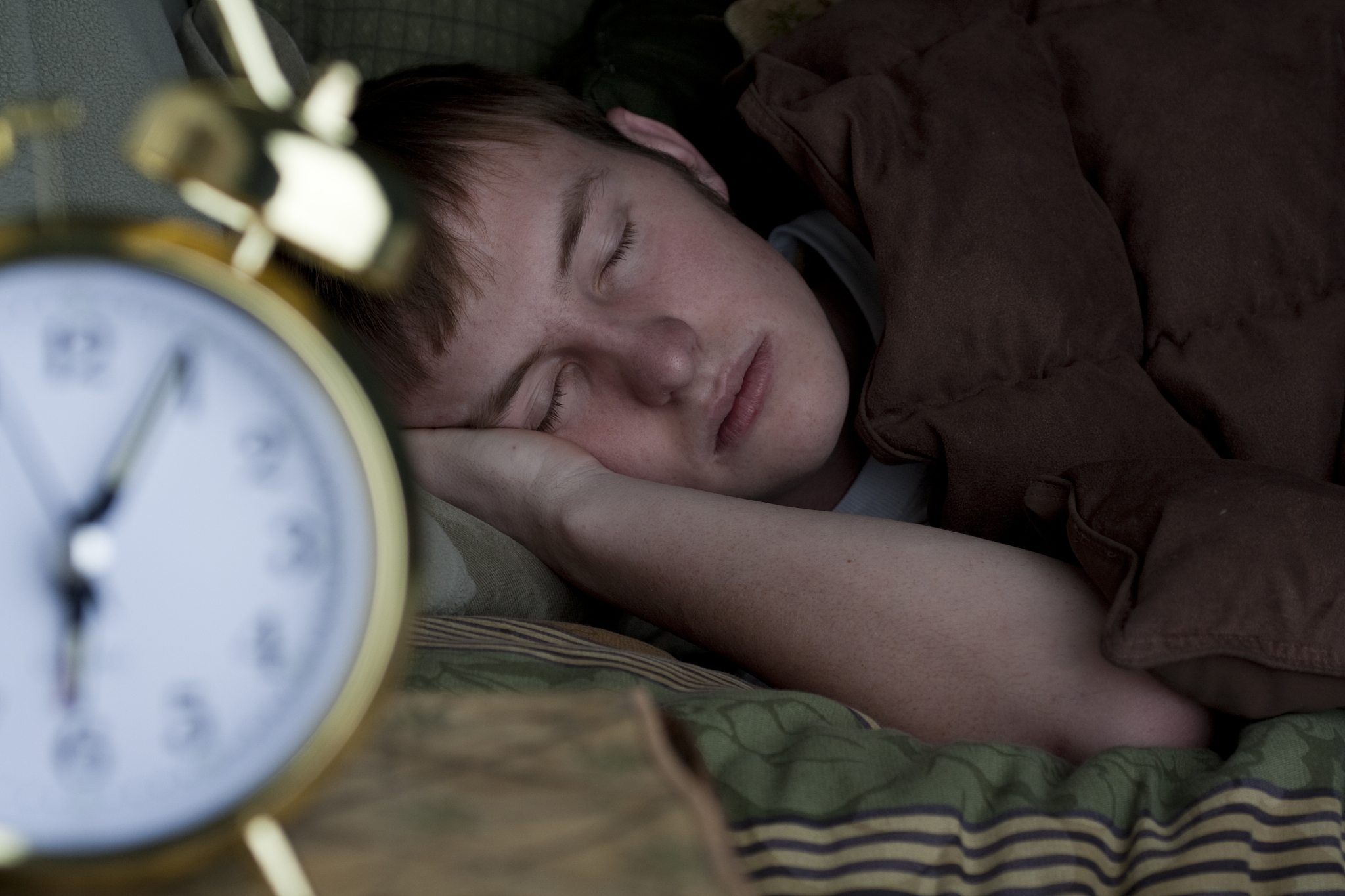 sleeping teenage boy with alarm clock