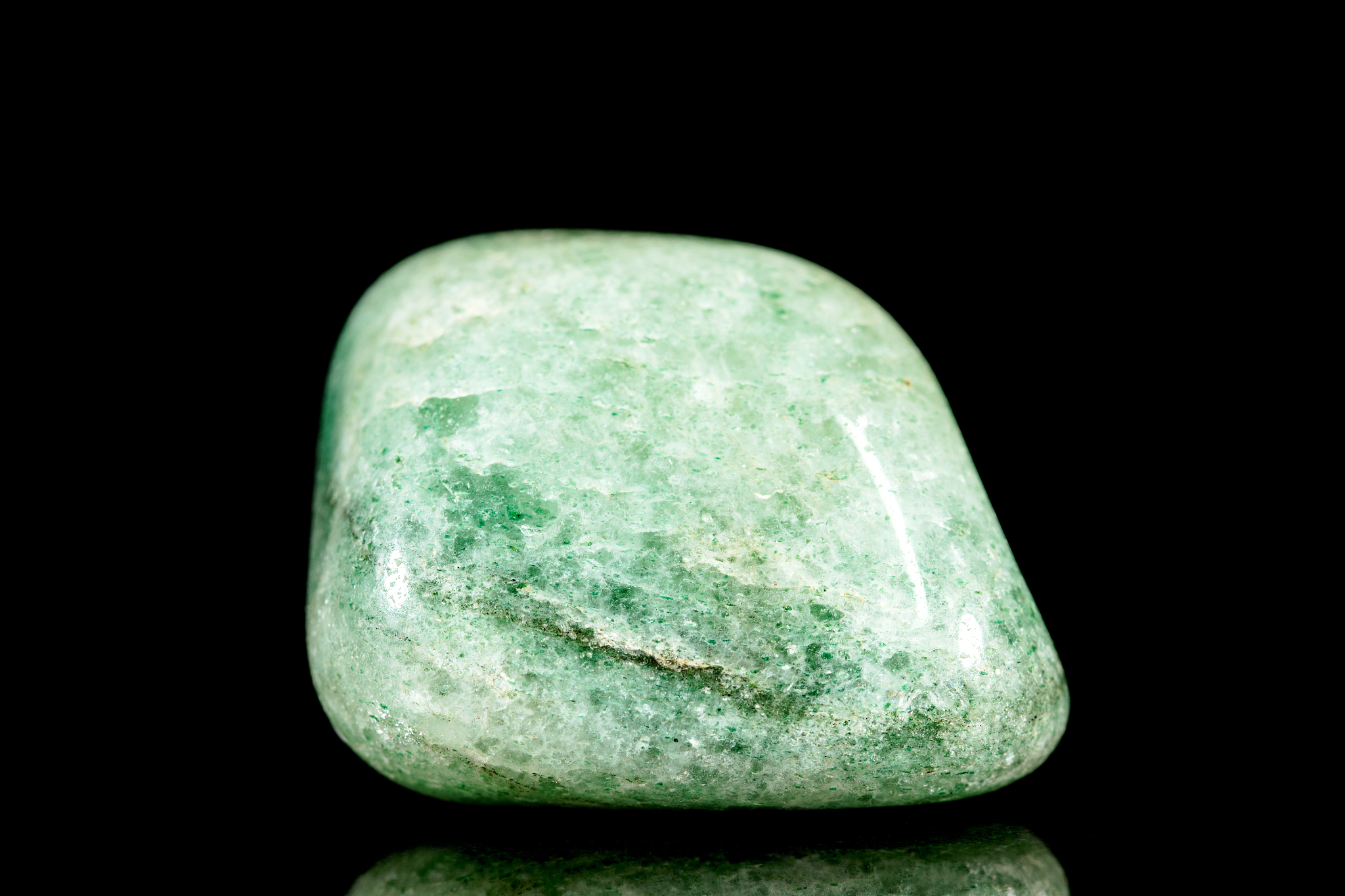 trumbled green jadeite mineral stone in front of black backgroun