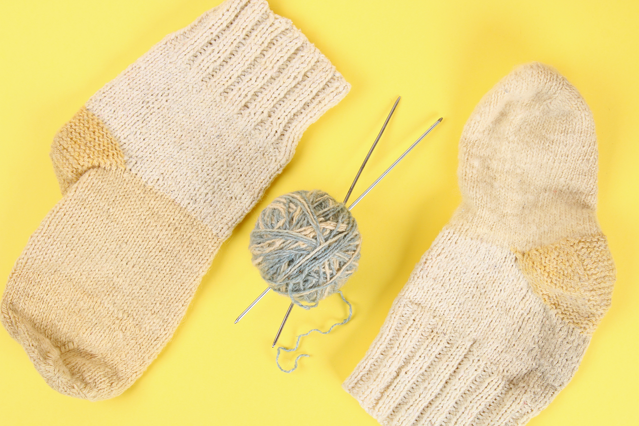 a ball of wool with knitting needles and knitted socks on a colo