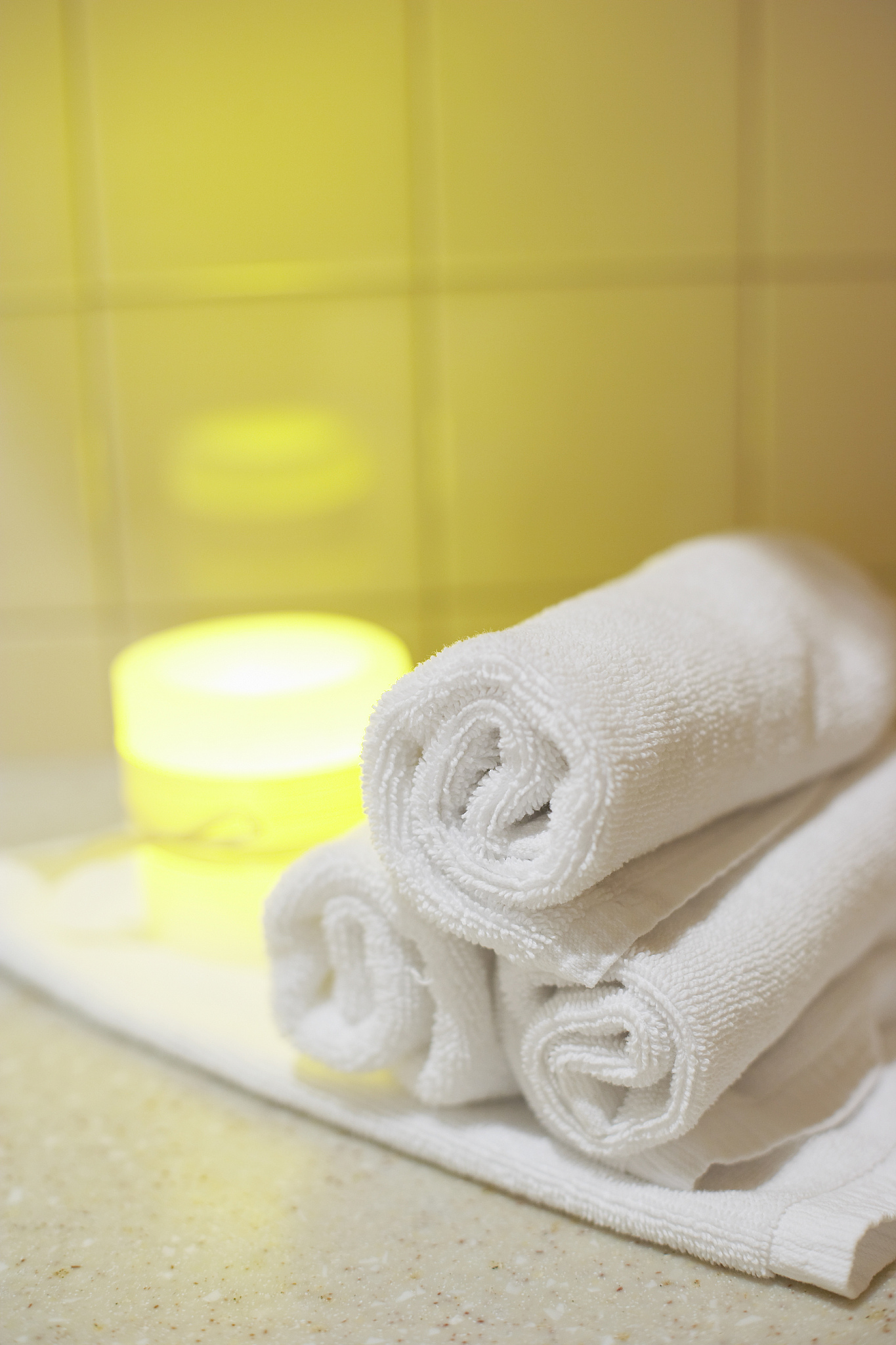 rolled towels and candle by tile wall