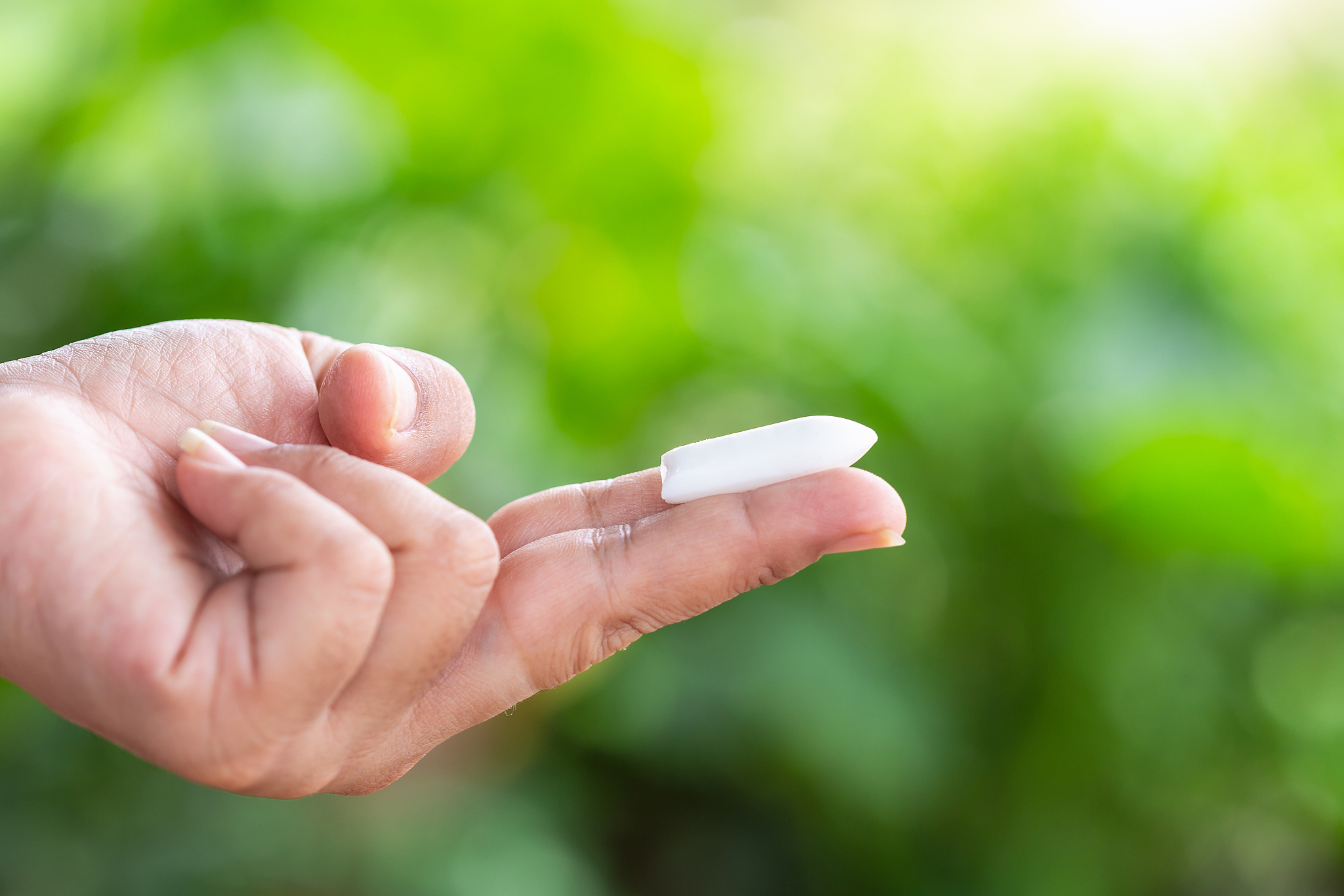 hand holding suppository candle on green nature light blur backg