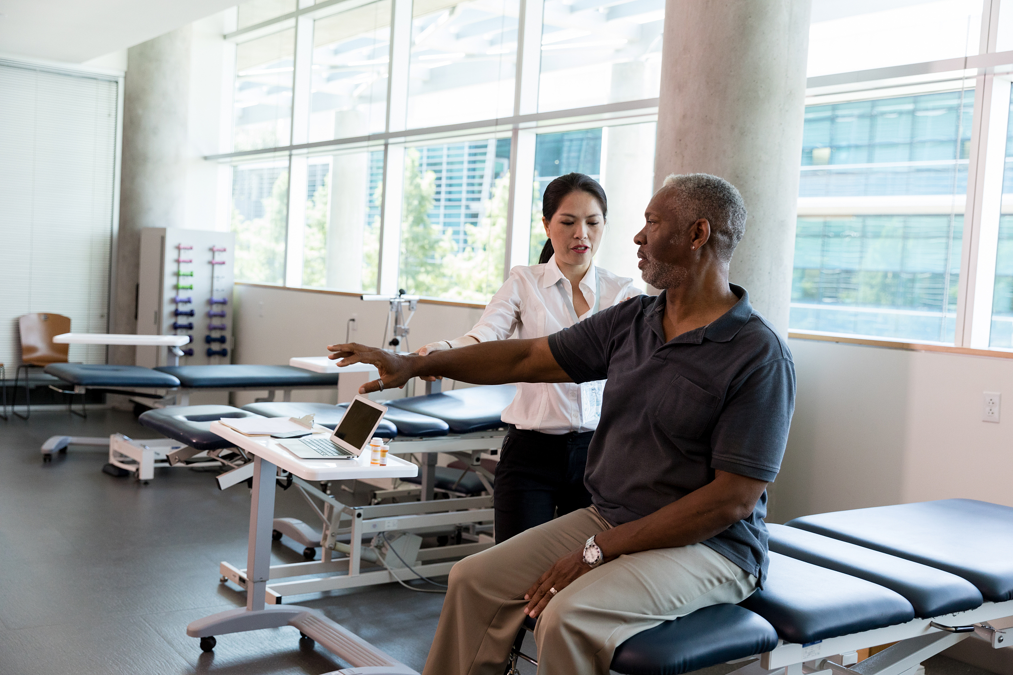 mid adult female physical therapist helps mature patient with st