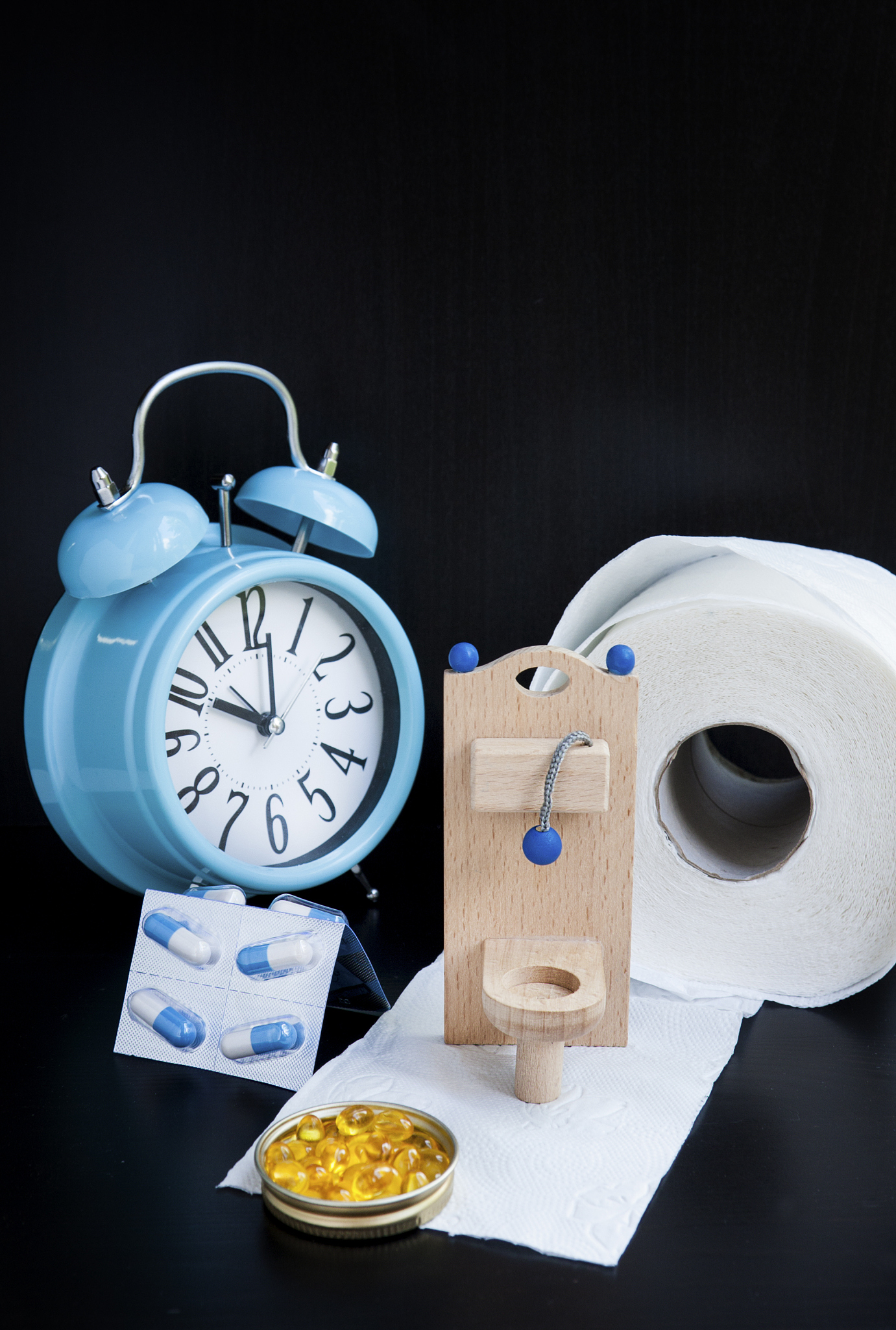 wooden toy toilet, pills and alarm clock on black