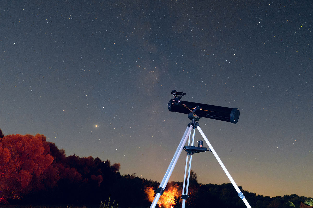 三脚架上的黑色望远镜反射镜在繁星点点的夜空中.观察星空.