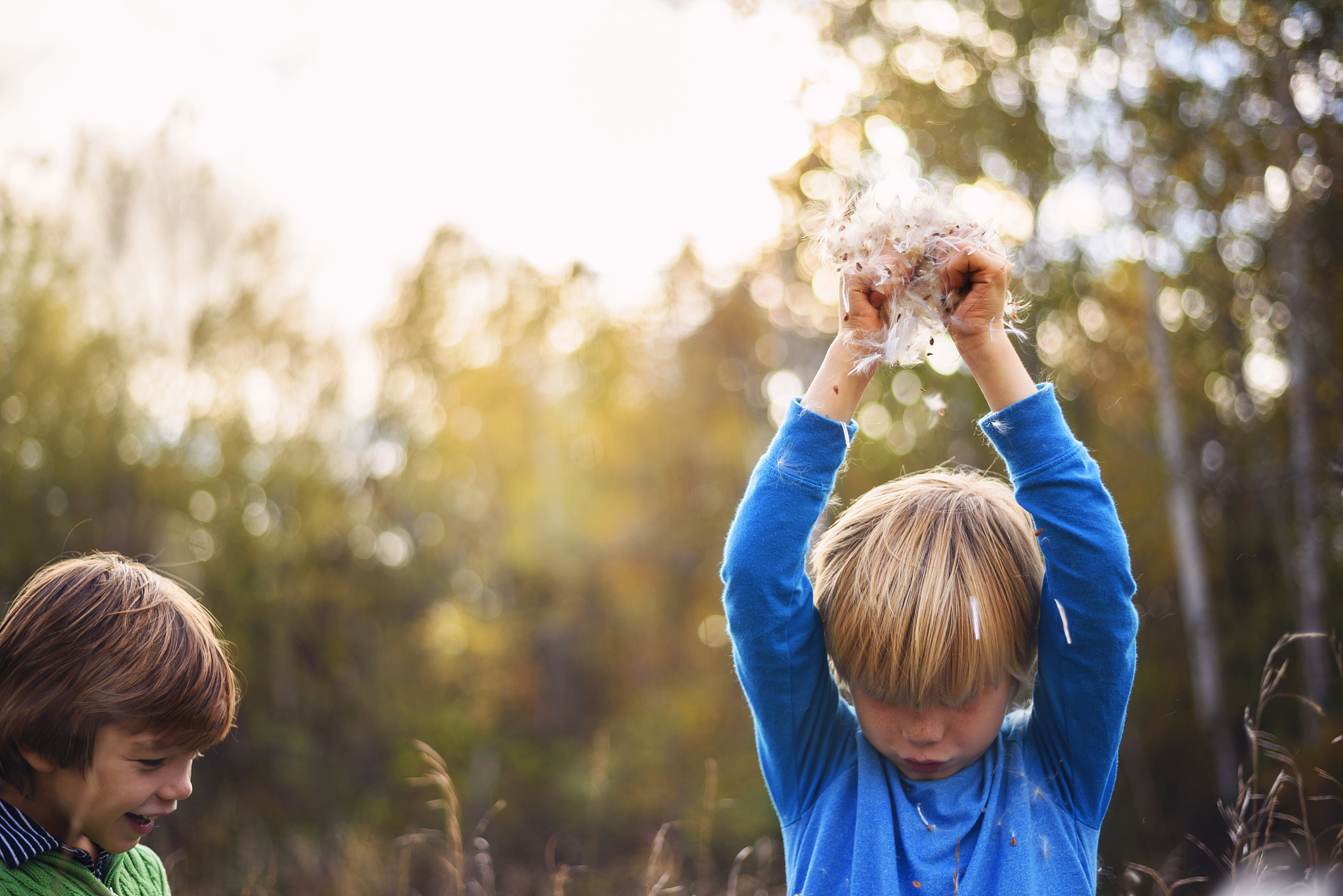 two boys standing in a  field playing with milkweed flowers
