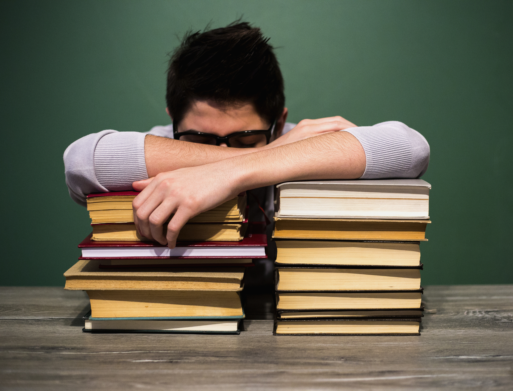 young man sleeping with books at table in room