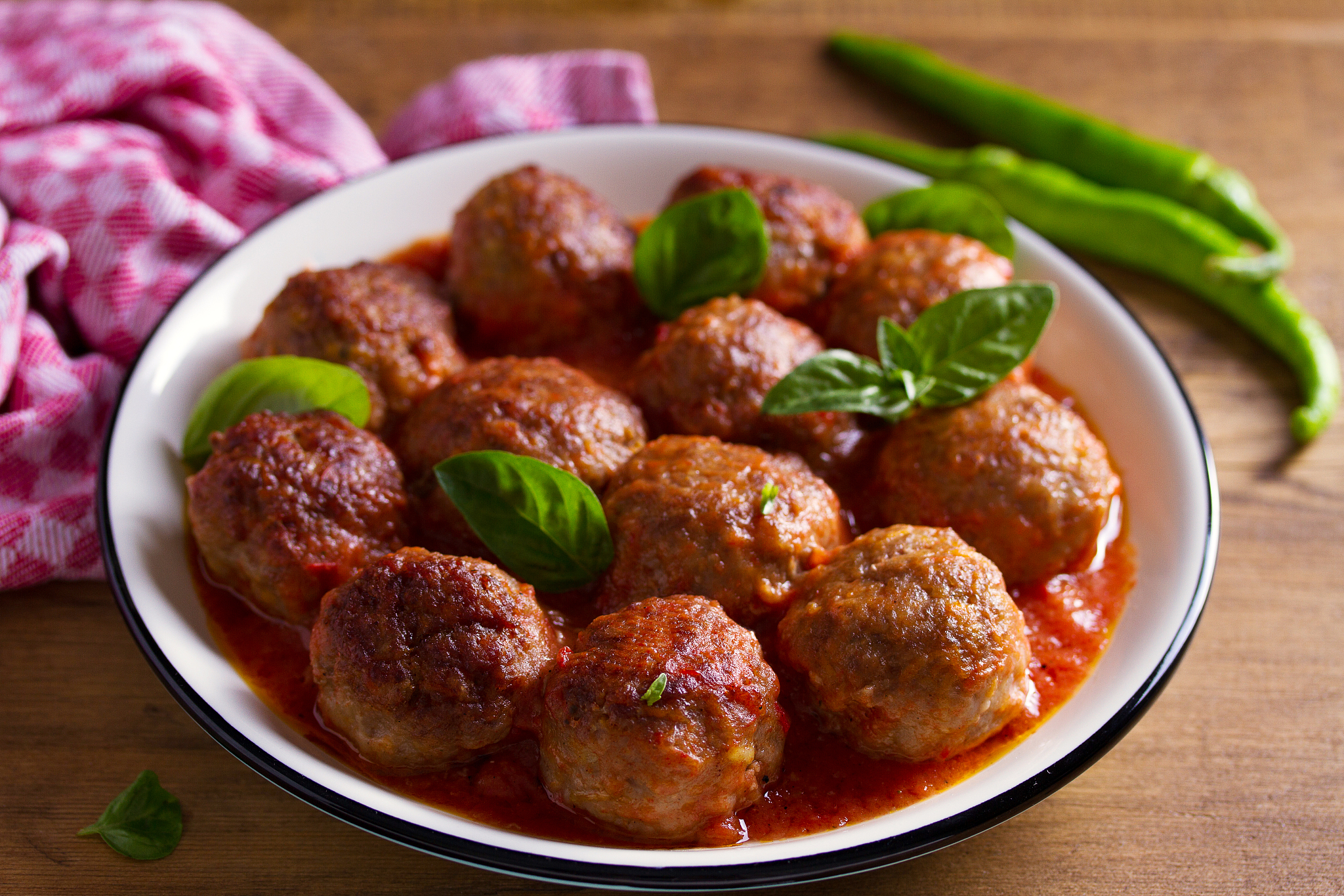 meatballs in tomato sauce, garnished with basil in bowl on woode