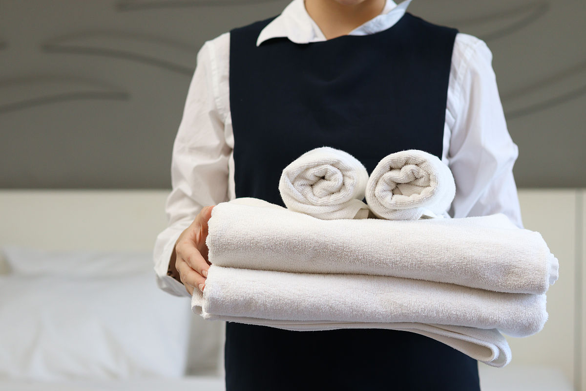 客房服务女佣清洁和整理床酒店房间概念,女客房服务员拿着一叠新鲜的
