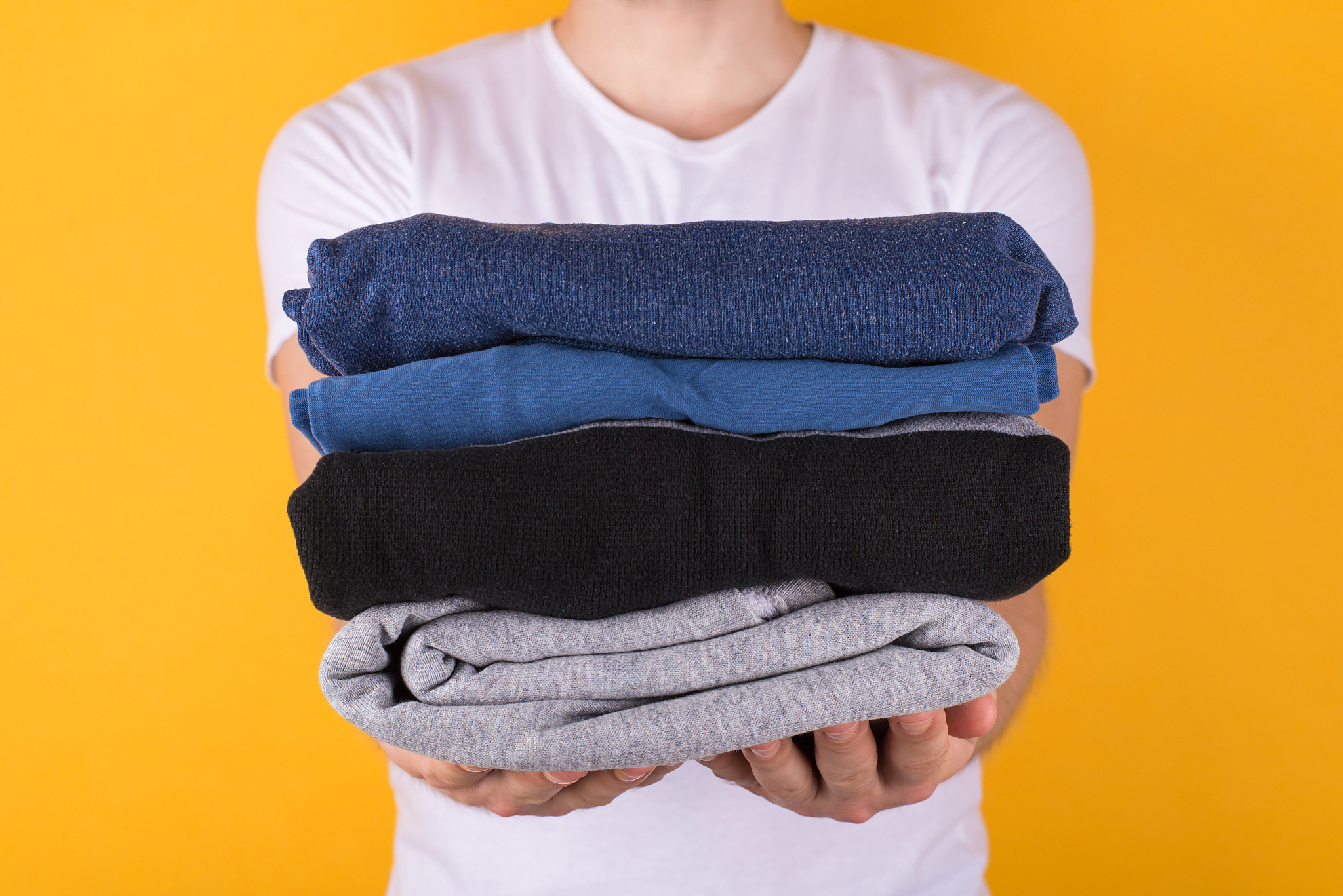 cropped front view photo of man holding folded clothes giving yo