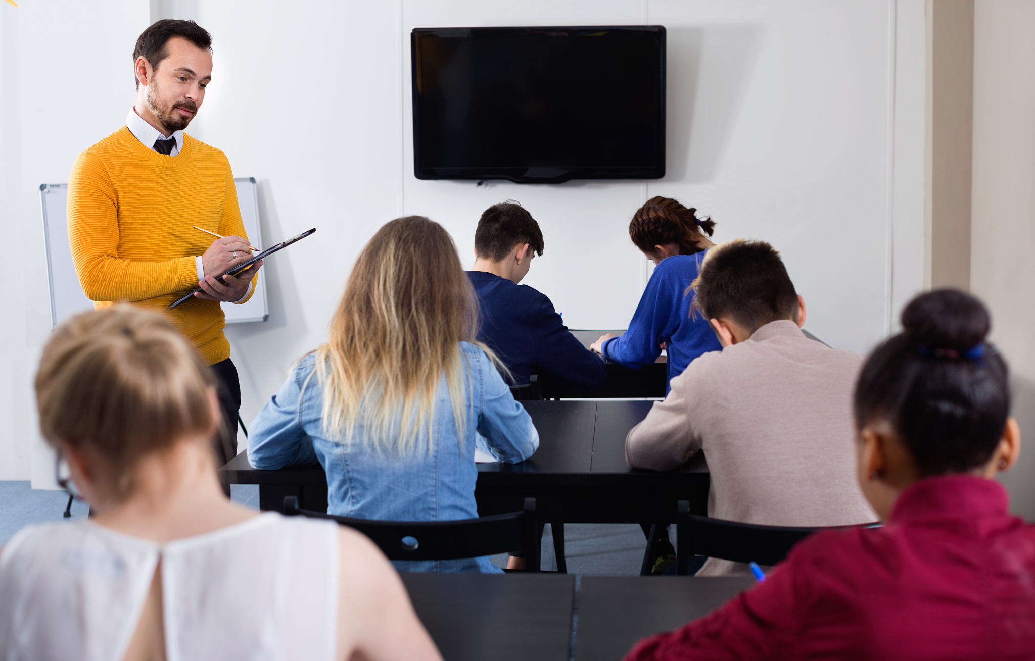 teacher monitoring students work during examination test in clas