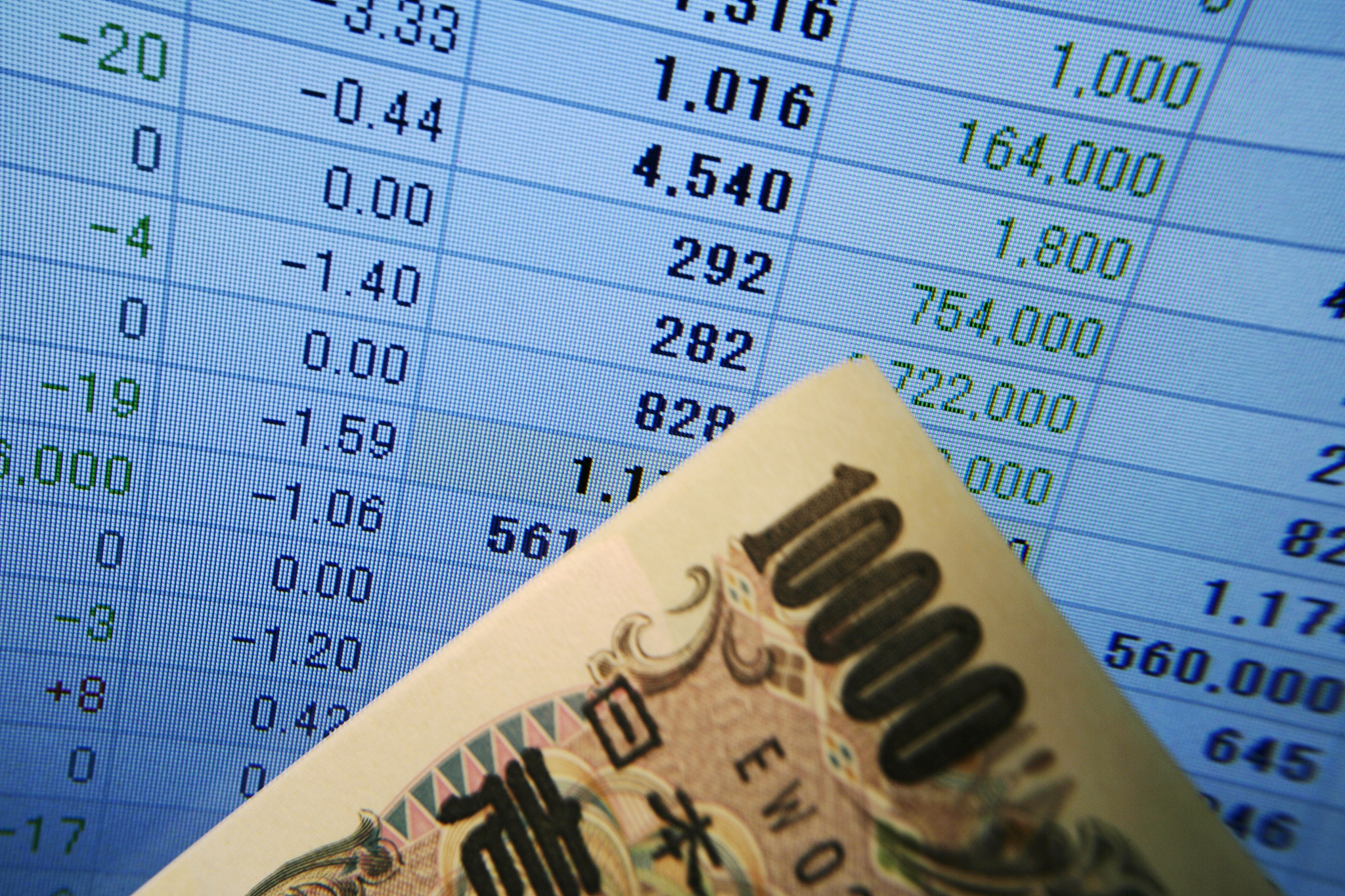 10, 100 yen bill in front of computer screen displaying financia