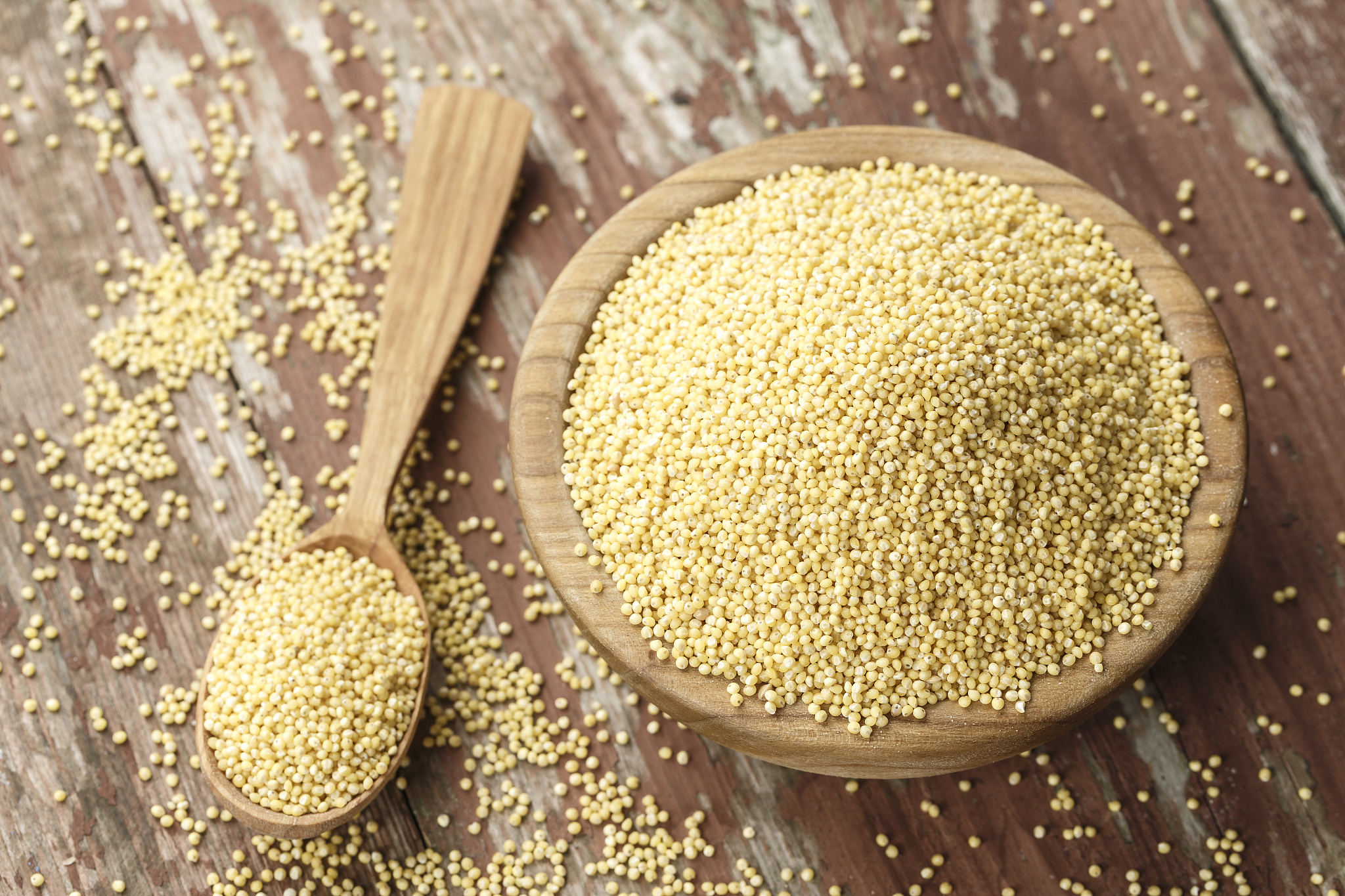 raw millet cereal in a wooden plate on a wooden background, next