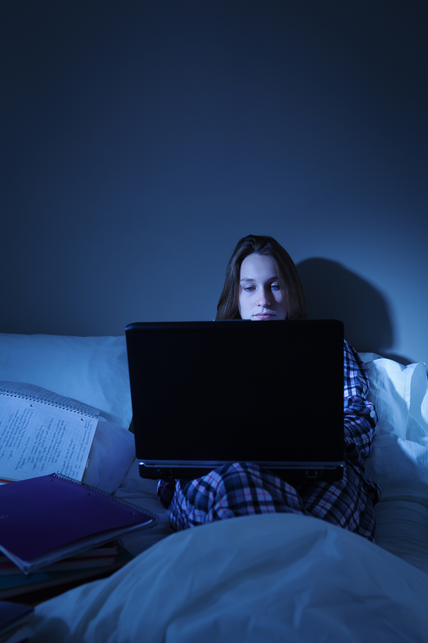 student working late at night in her dorm room bed