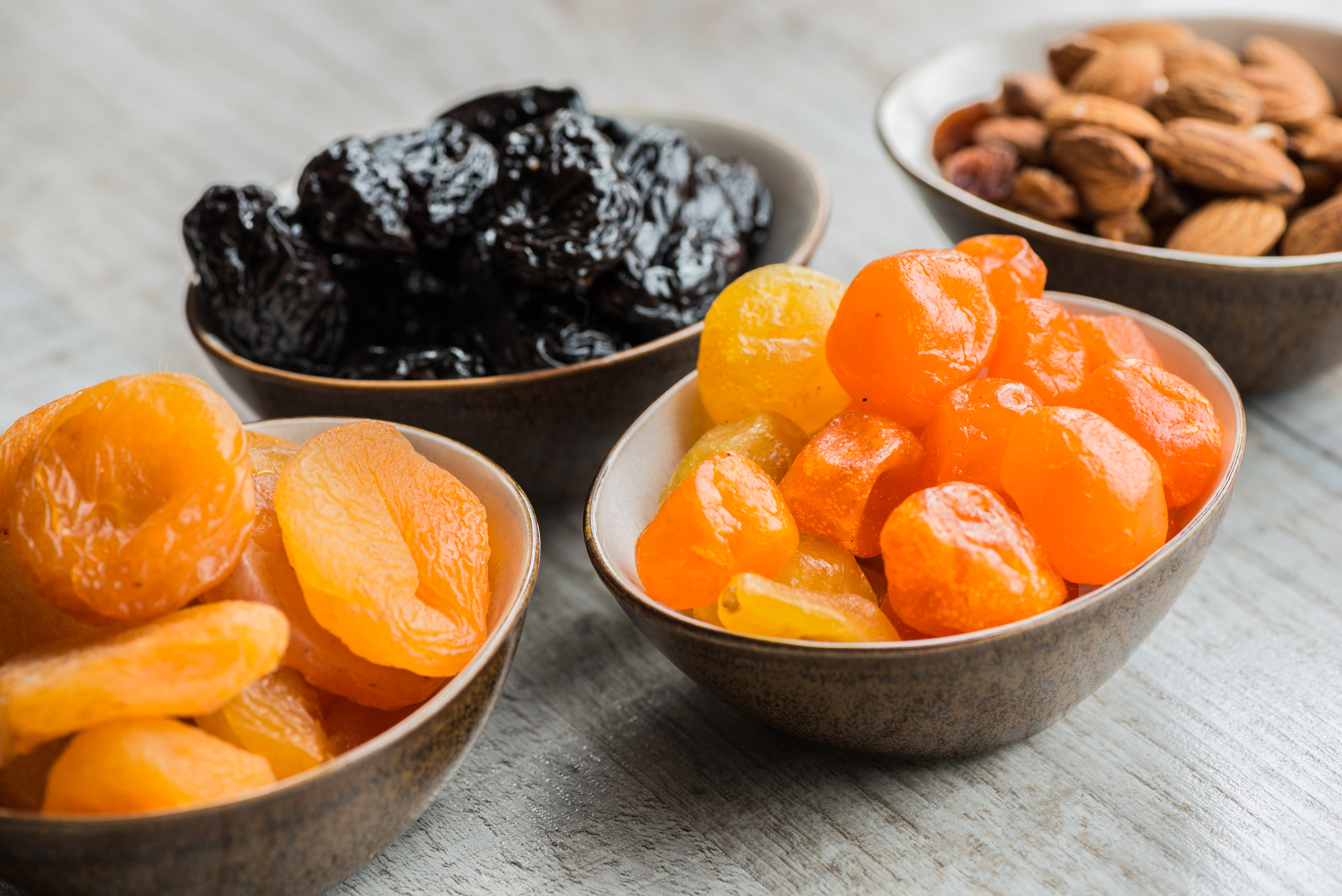four plates with dried fruits on wooden background: dried mandar