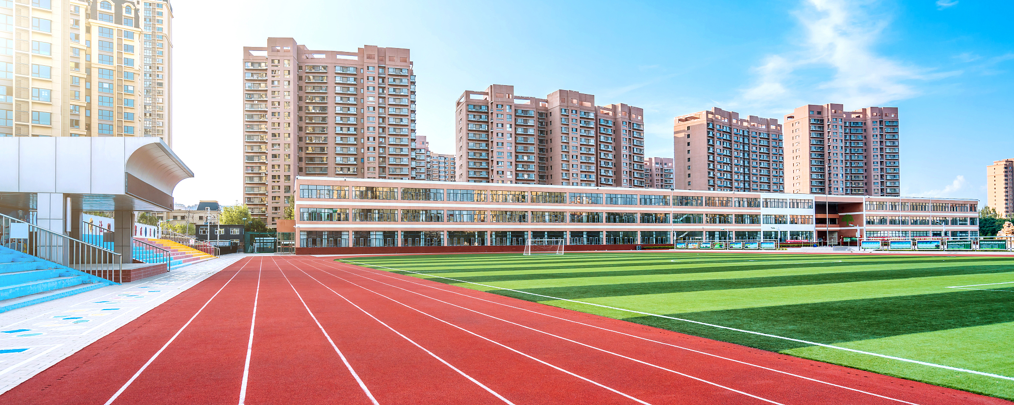 阳光下的体育场红色跑道和远处的高楼建筑