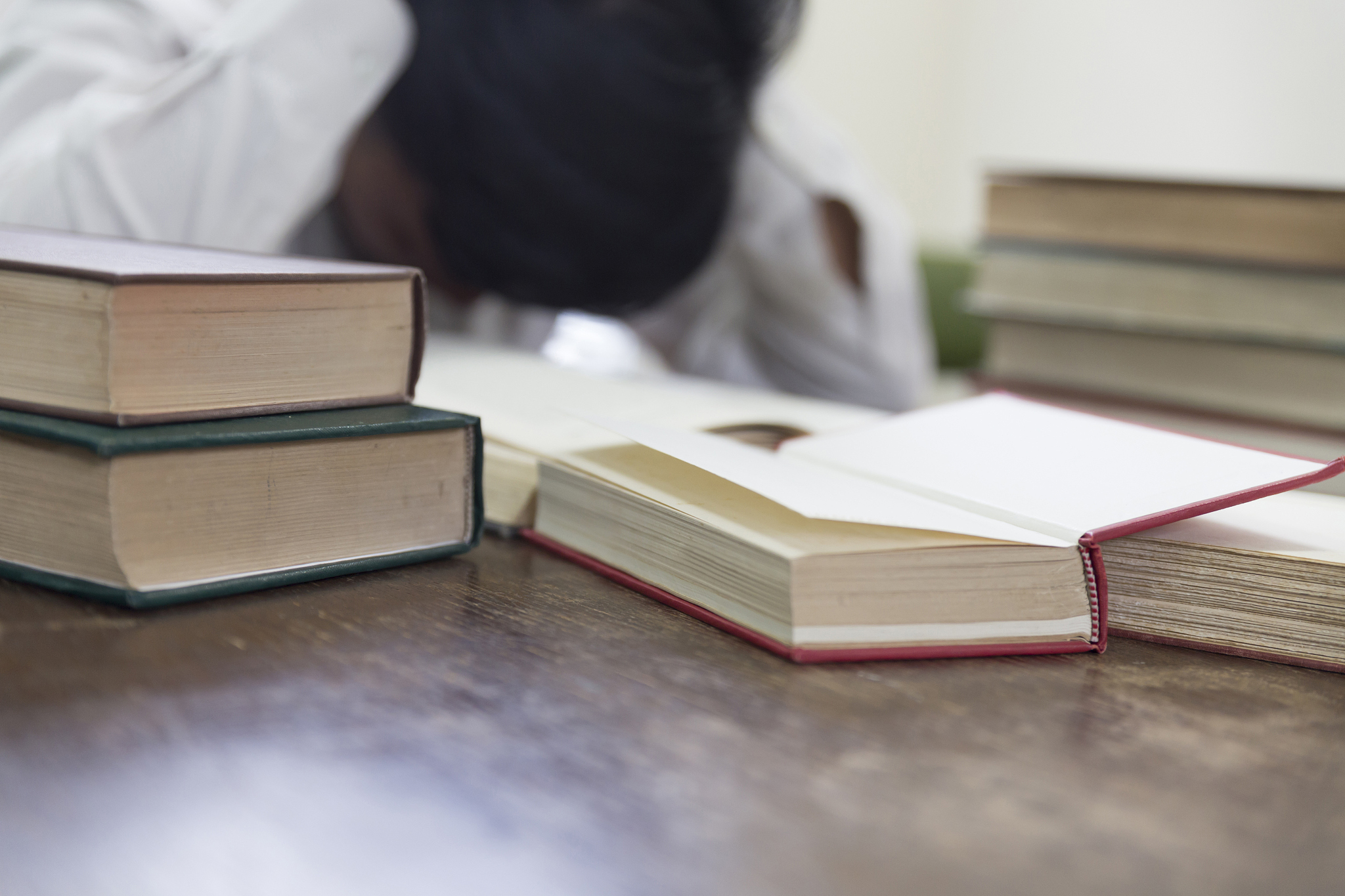 confused and frustrated man with textbook stack on wooden desk