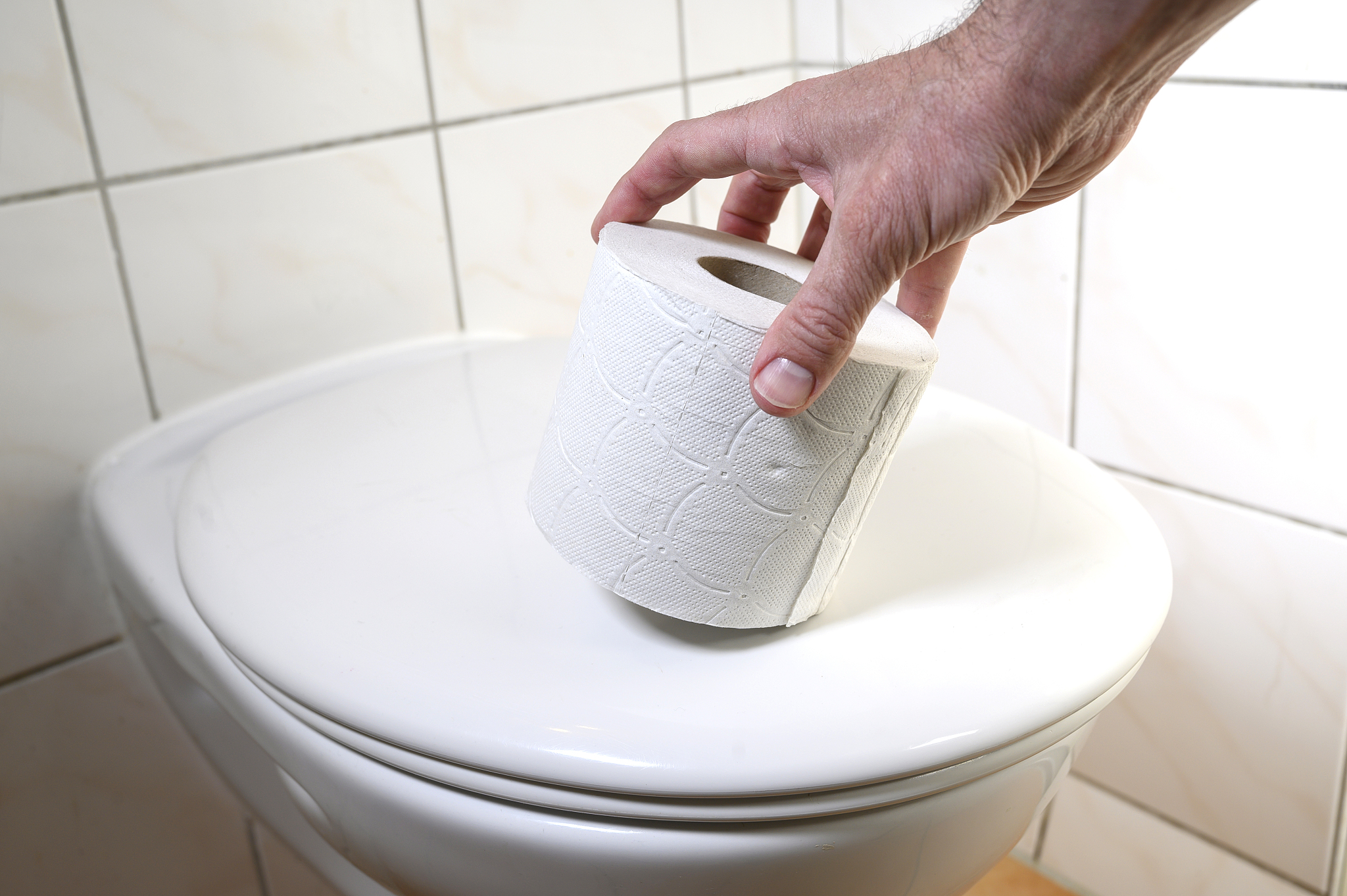man's hand taking a roll of toilet paper which is on the toilet 