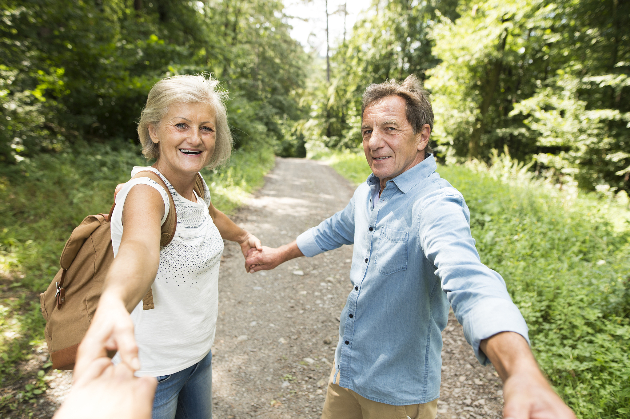 senior couple holding hands with third person on forest track