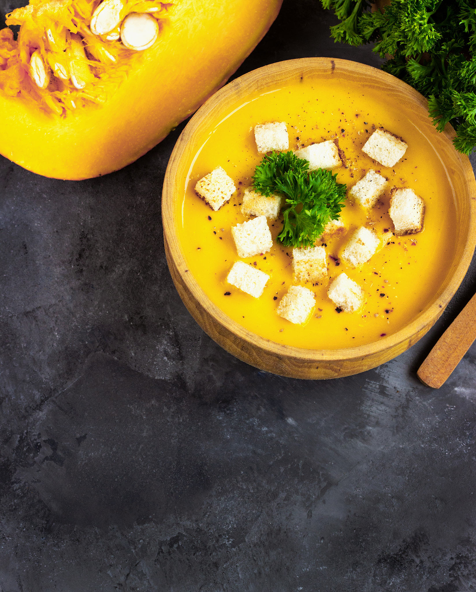 pumpkin soup with cream, bread and fresh parsley in a rustic met