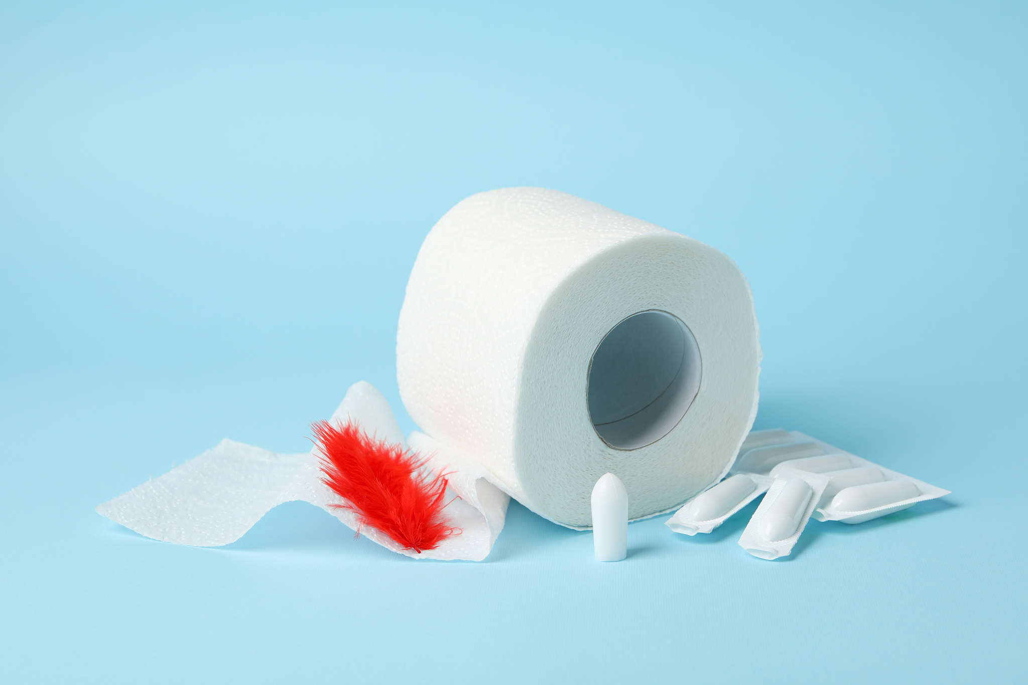 toilet paper, feather and candles on blue background. hemorrhoid