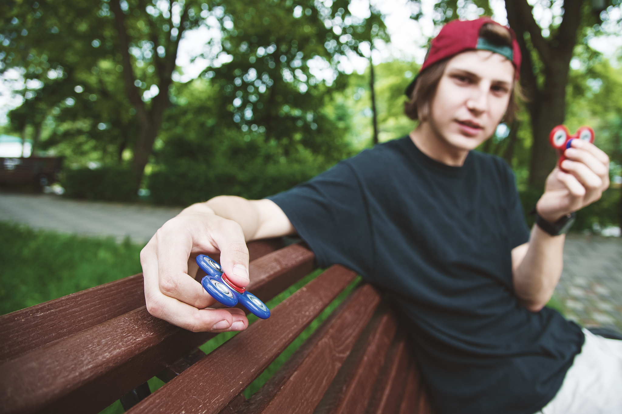 a long-haired hipster in a cap sits on a bench and spins a fidge