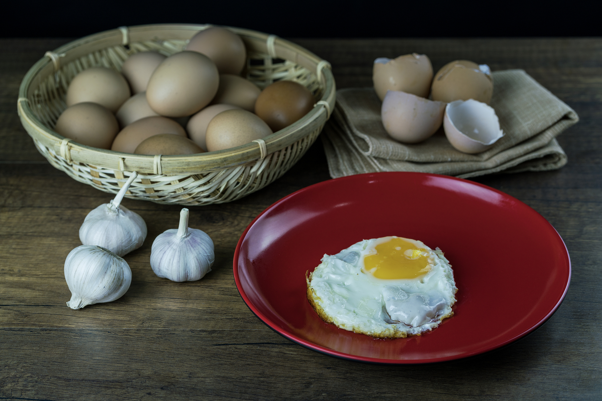 fried egg and eggs in the basket with egg shell on the wooden ba