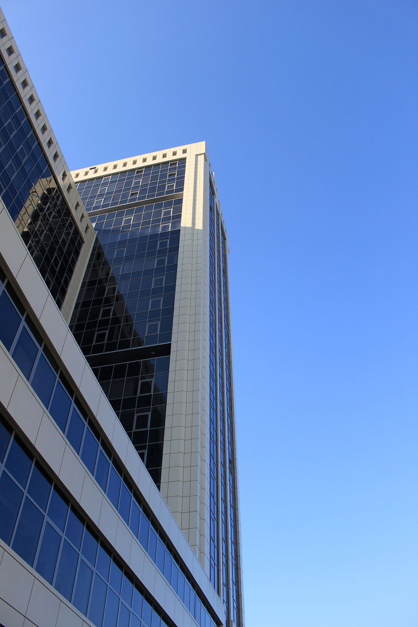 润色以下句子：在城市的北方矗立着一栋高耸入云的建筑大楼——银河白岱大厦。据说这是银河队的两个总部大厦之一大楼外墙均用蓝色玻璃幕墙进行装潢这种蓝色的热反射玻璃外观上虽然极具美感但却无法散发出生机和活力反而让人感受到一种无形的压迫感给城市带来了一种低沉不详的气氛。