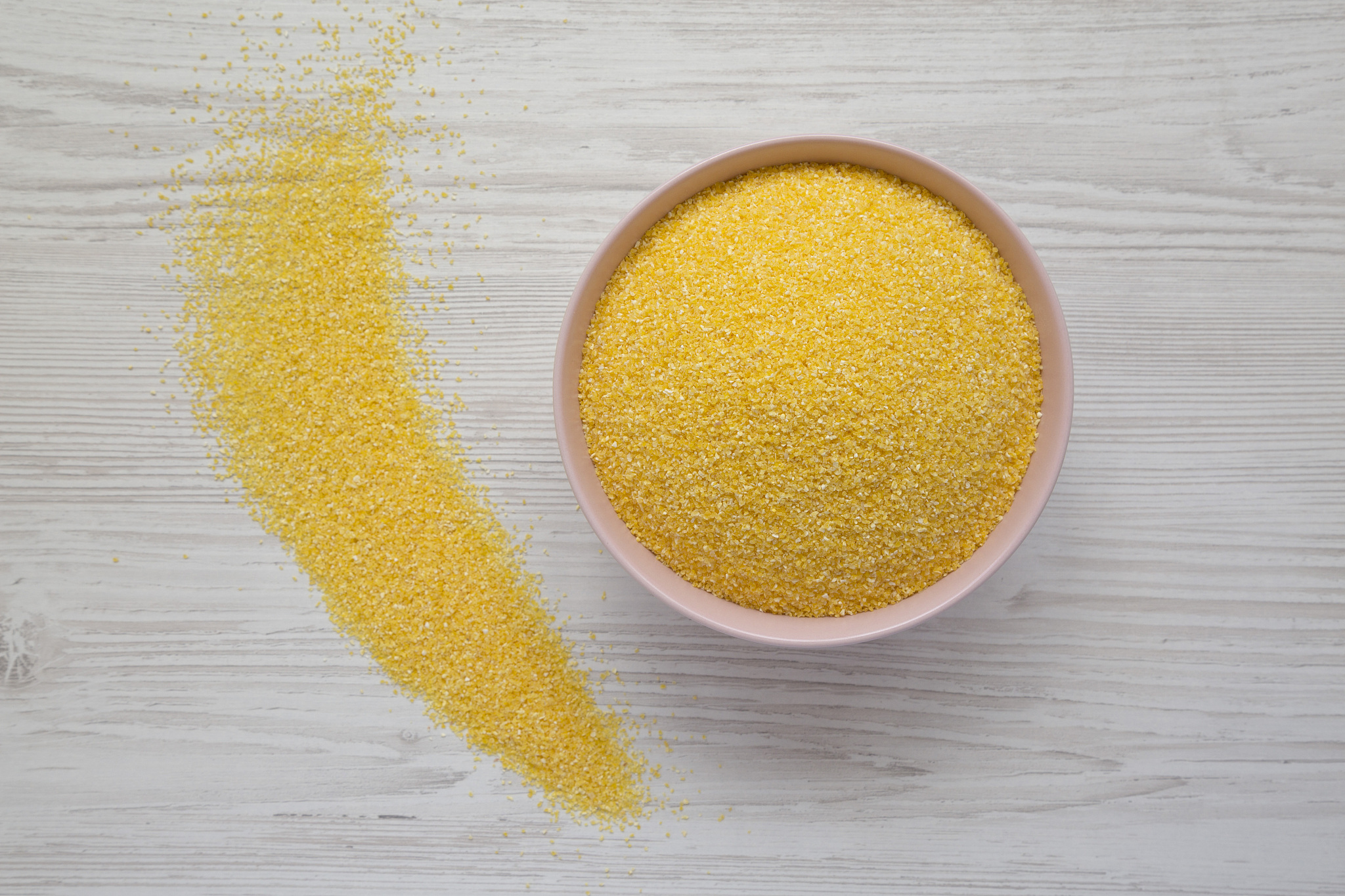dry organic masarepa corn meal in a pink bowl over white wooden 