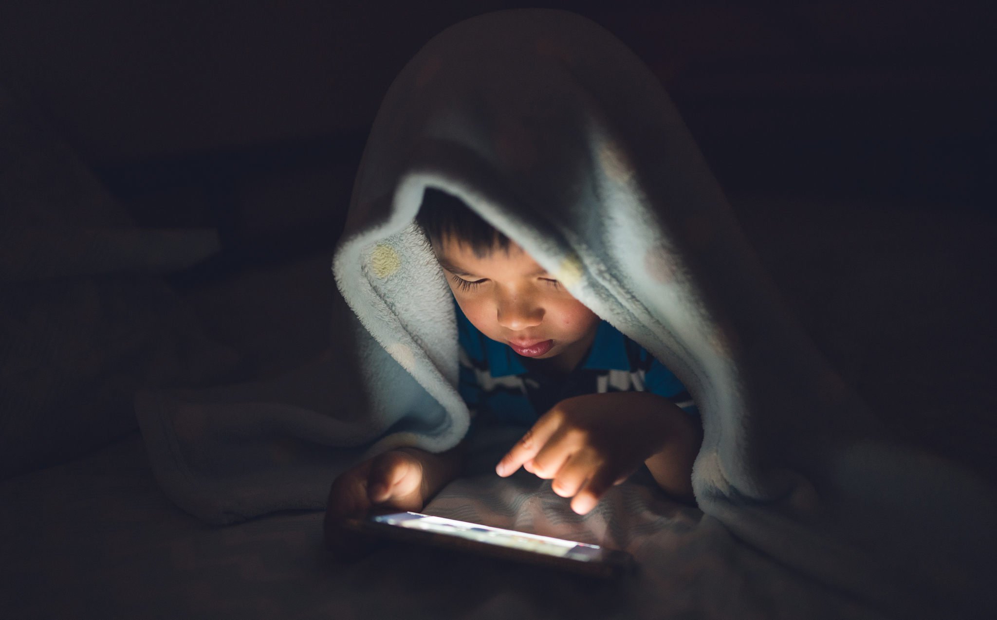 kid using smartphone on bed.