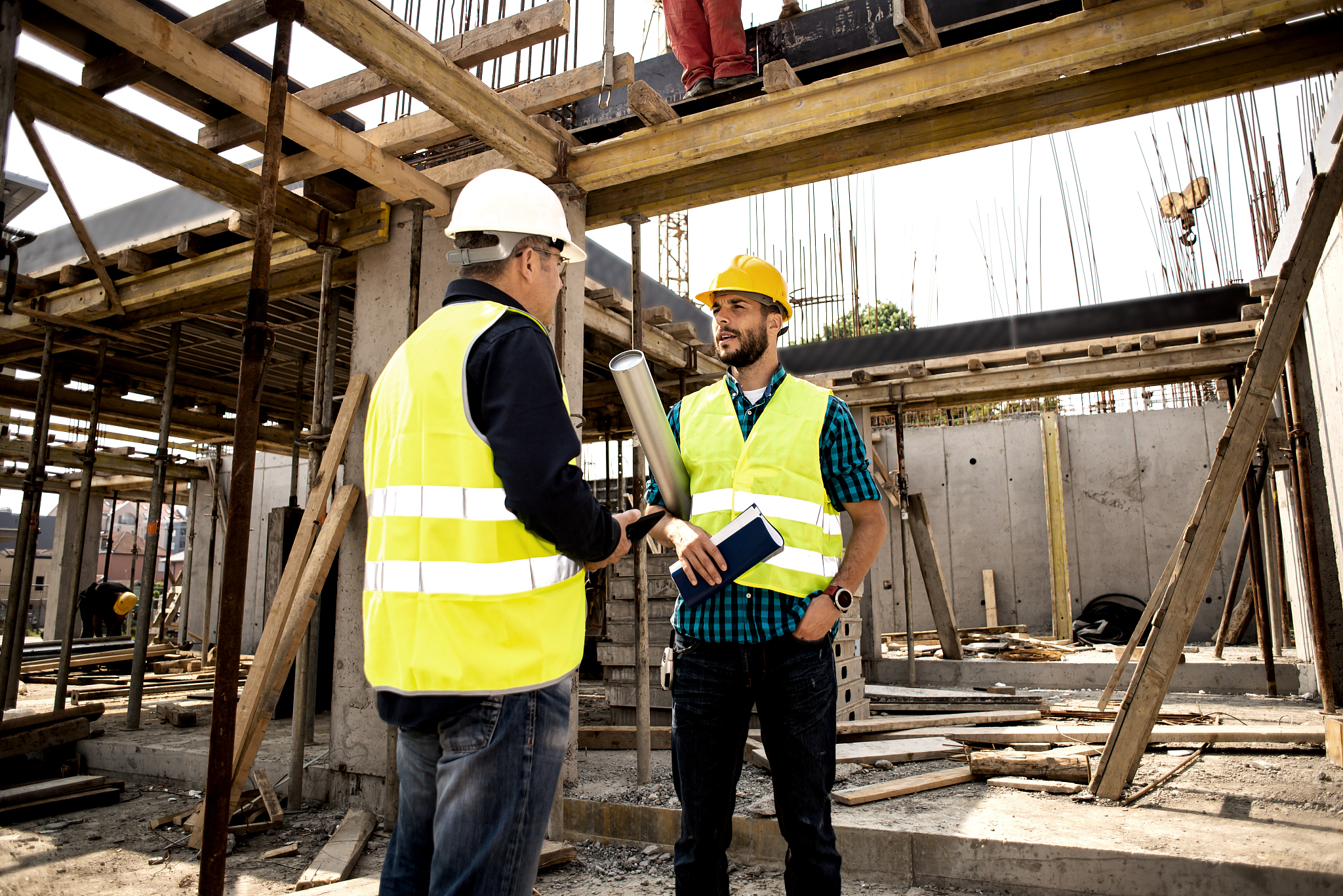 men in hardhat and green jacket posing on building site.