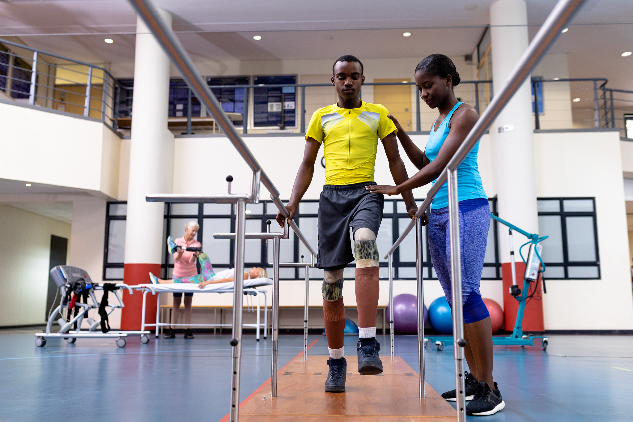 physiotherapist helping disabled man walk with parallel bars in 