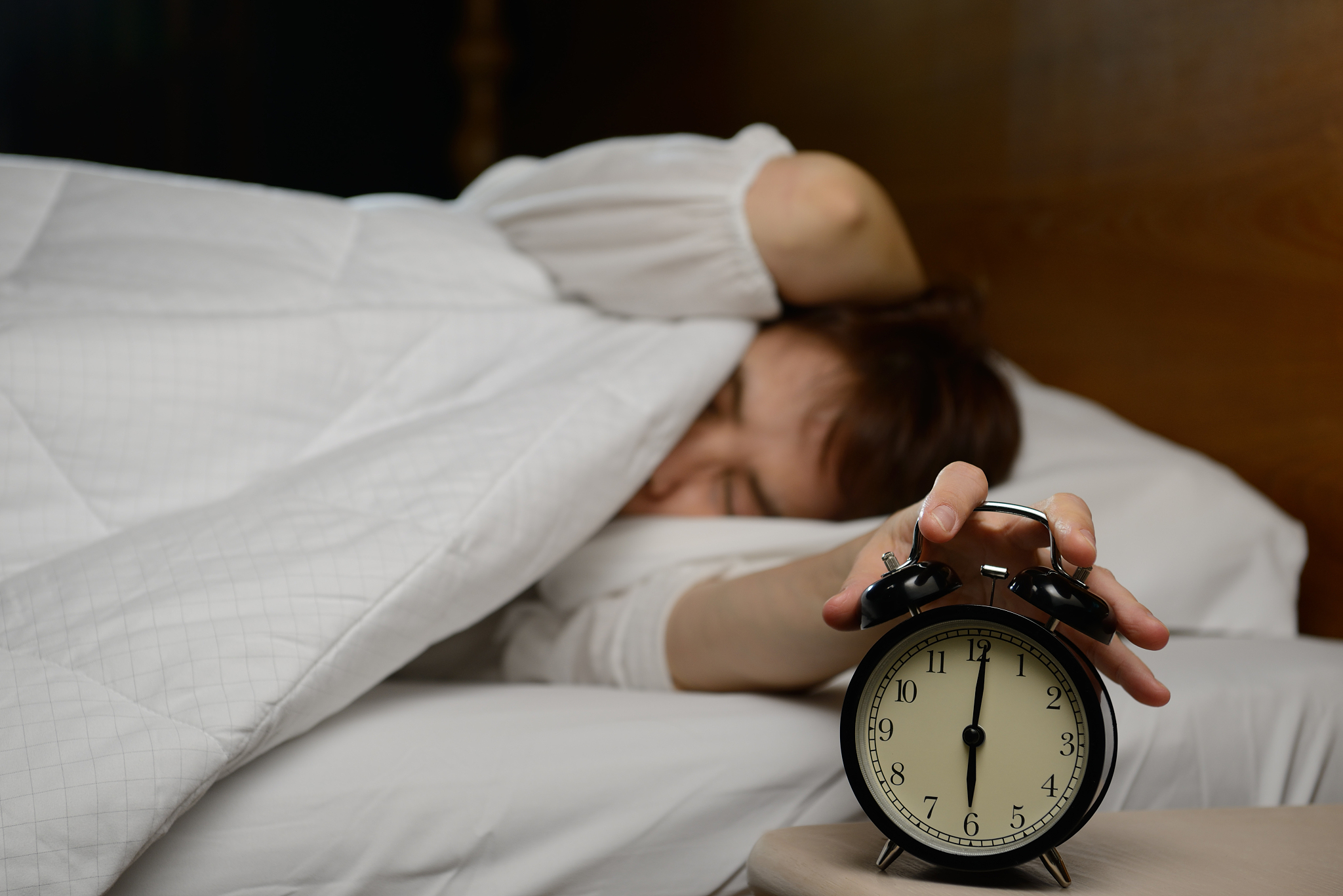 young woman turning off the alarm clock on the bed
