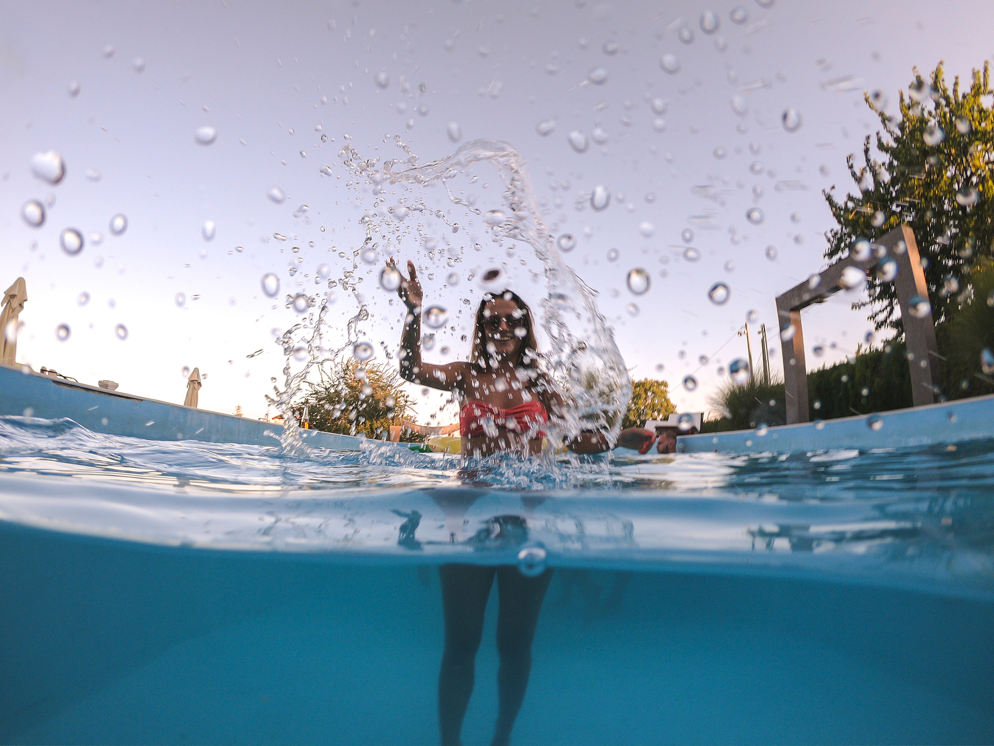 young woman splashing camera in pool