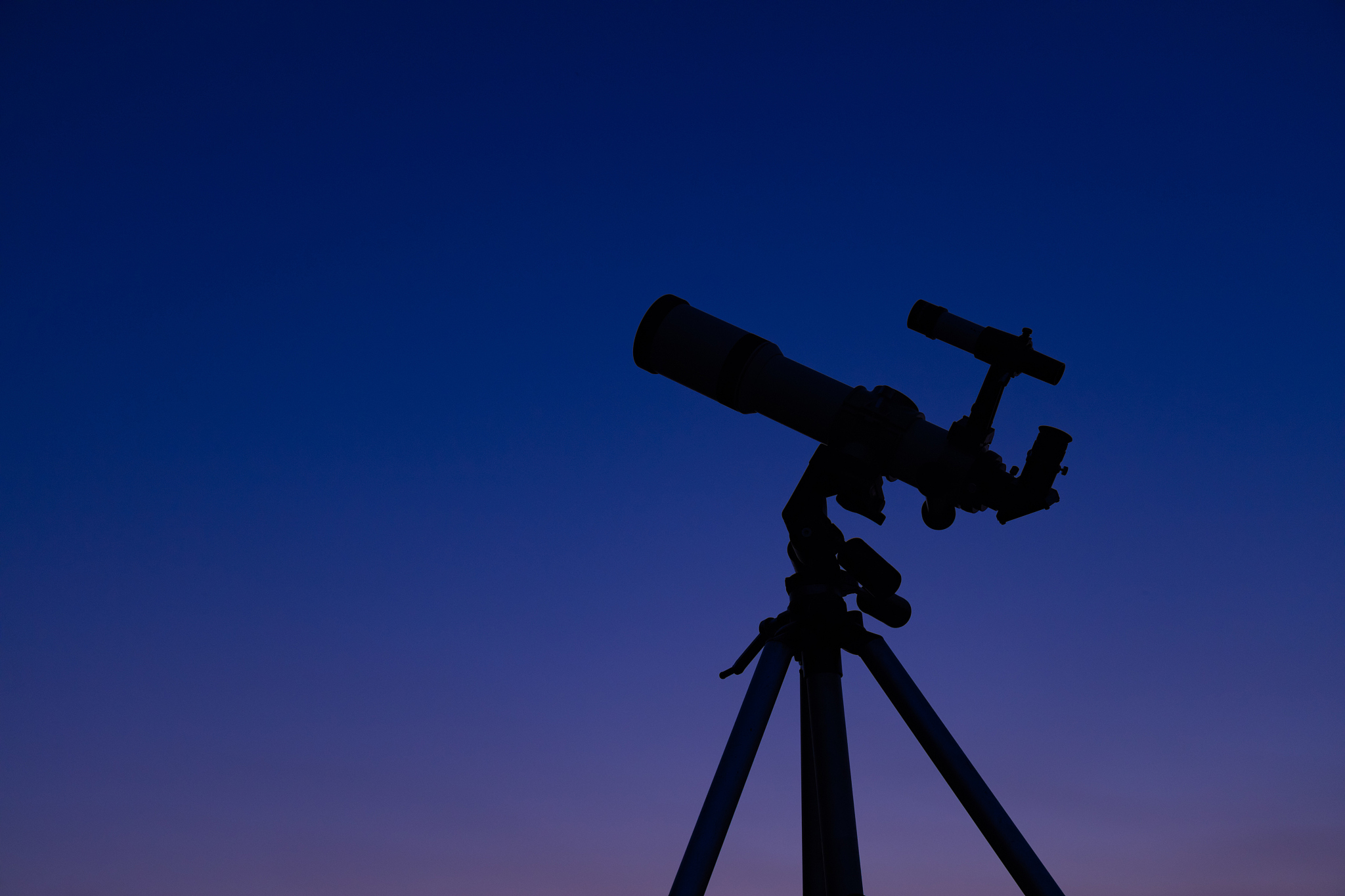 silhouette of a telescope with evening sky in the background.