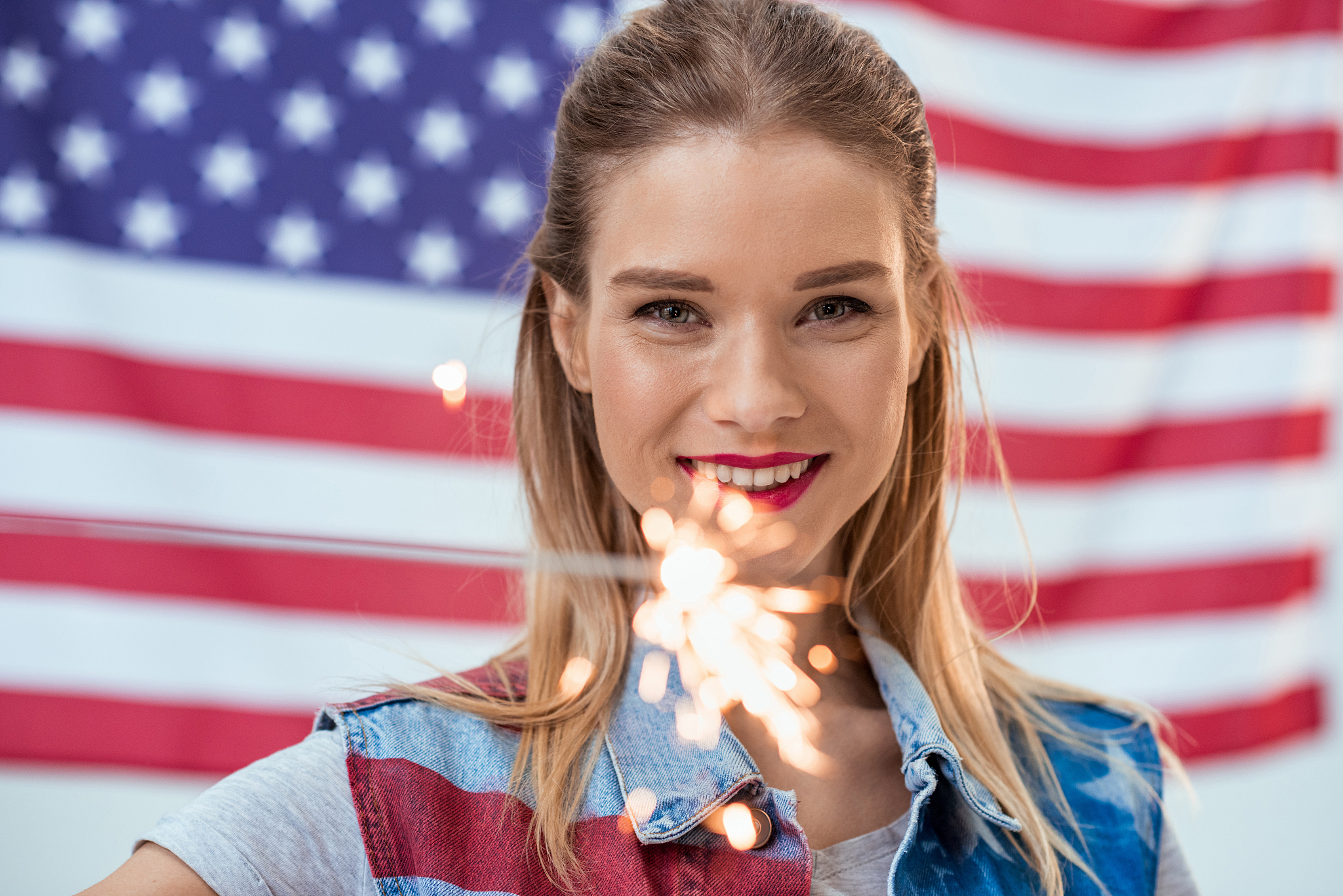 woman holding sparkler with american flag behind