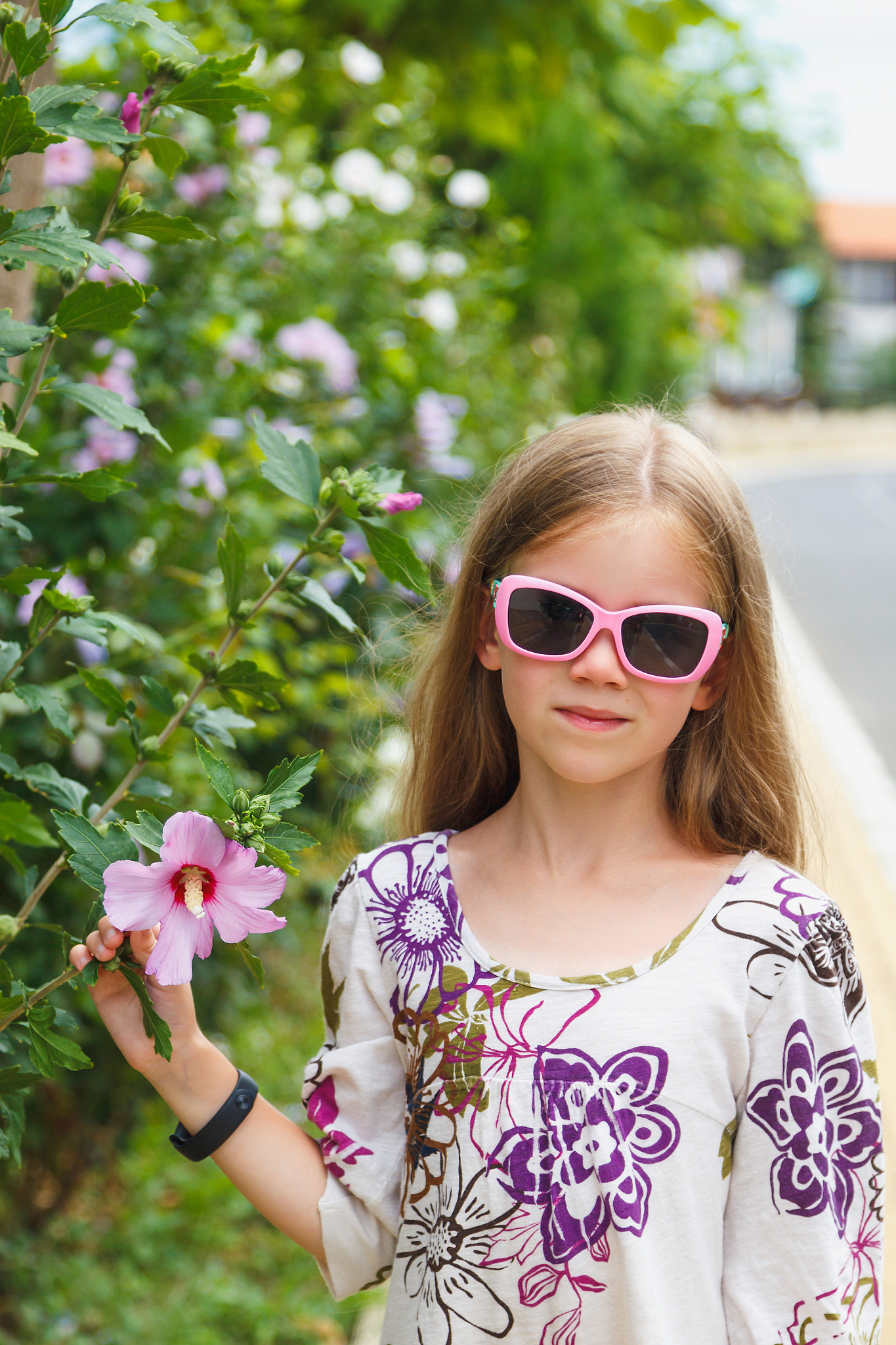 a girl near a bush with pink flowers.
