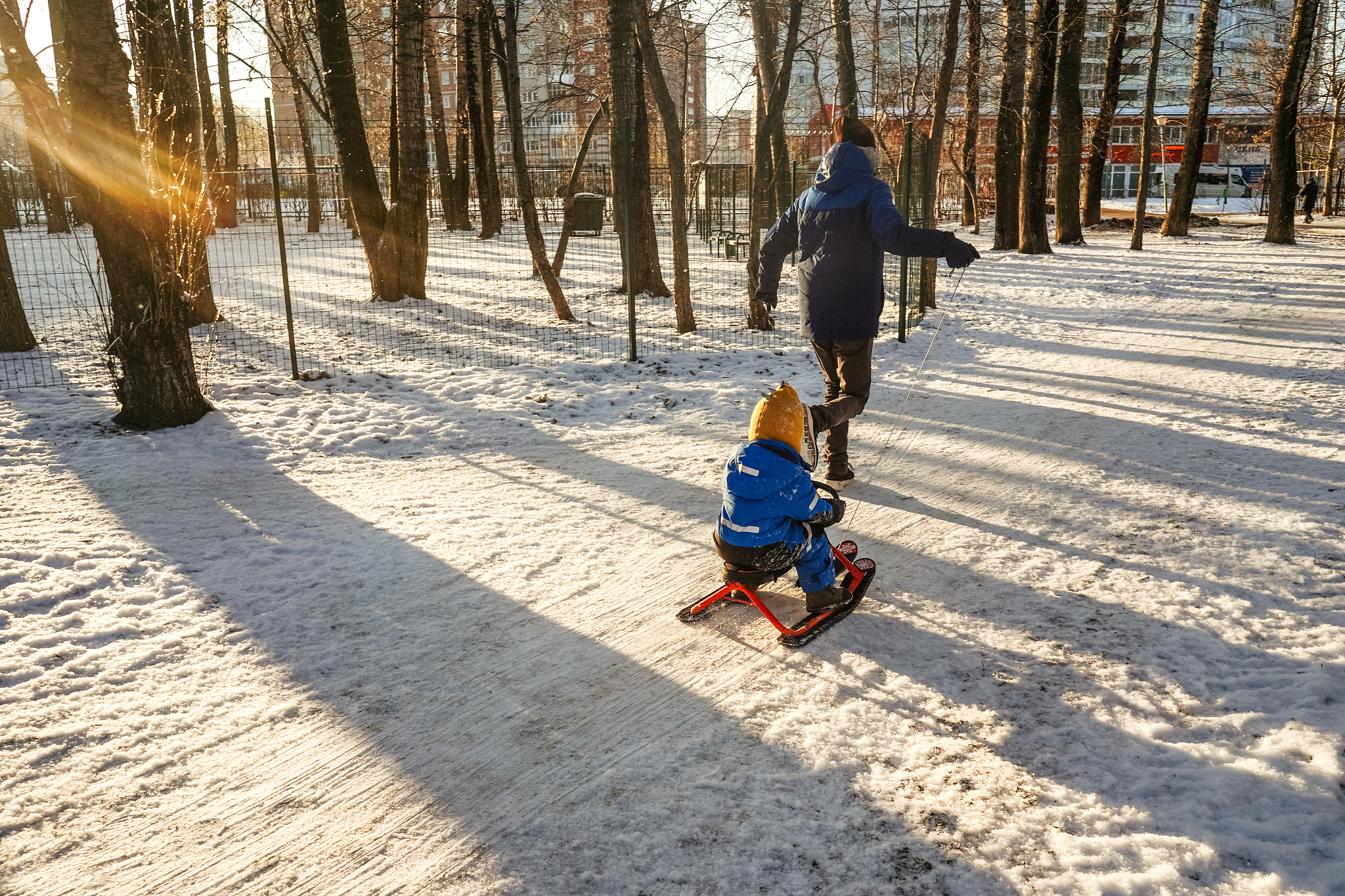 man rolls child on snowmobile in park.