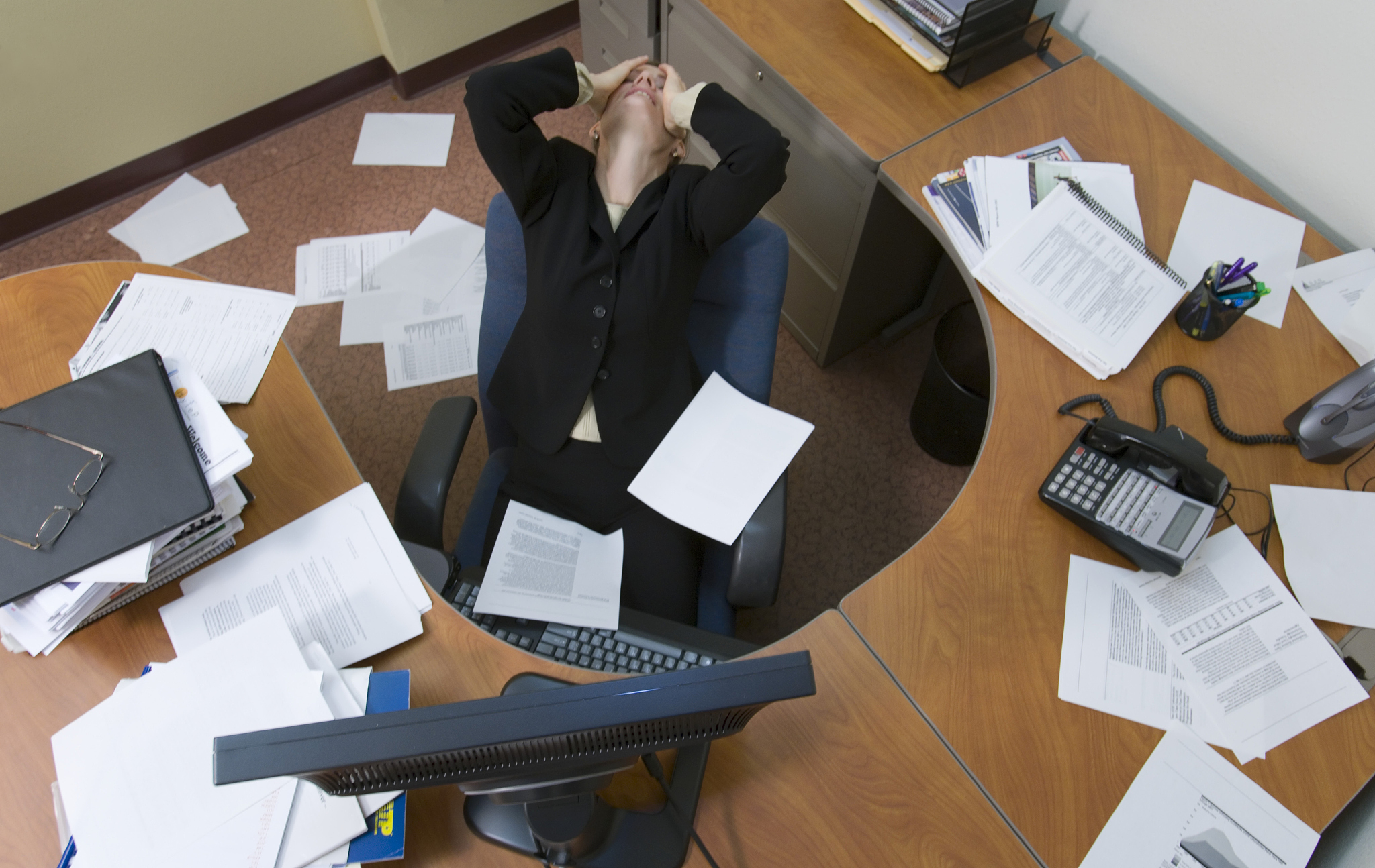 mature businesswoman leaning back, covering eyes, papers everywh