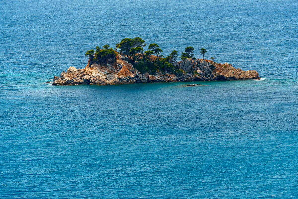 远海小岛的全景,有岩石,树木,蓝天,海水和海浪,夏日