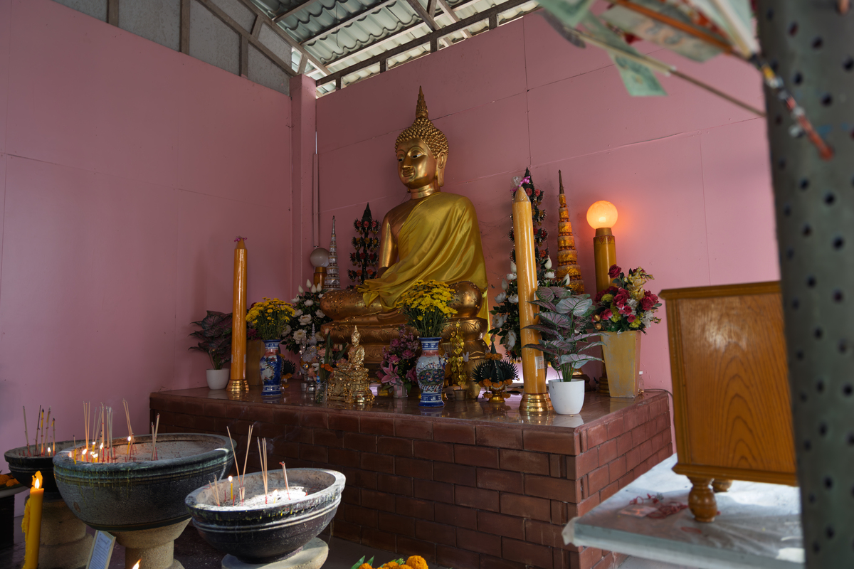 泰国佛教圣地金色佛像,周围环绕着蜡烛,香炉,鲜花供品