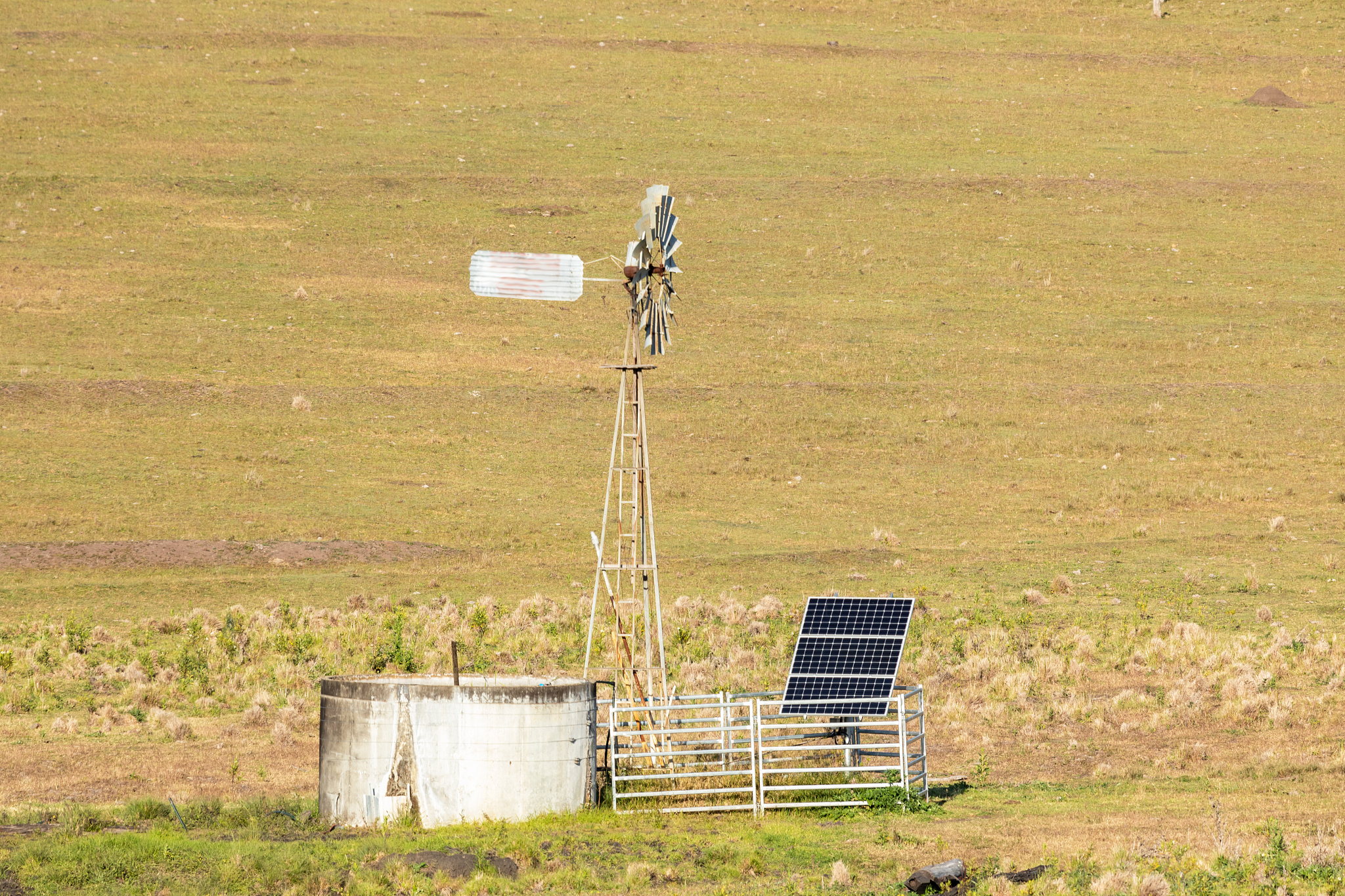 close up view of a windmill out in the country with solar panels